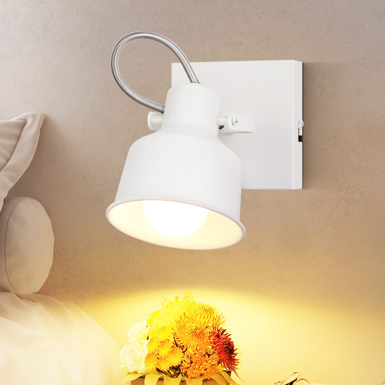 Biała lampa ścienna z elastycznym ramieniem. Pod światłem znajduje się kompozycja kwiatowa.