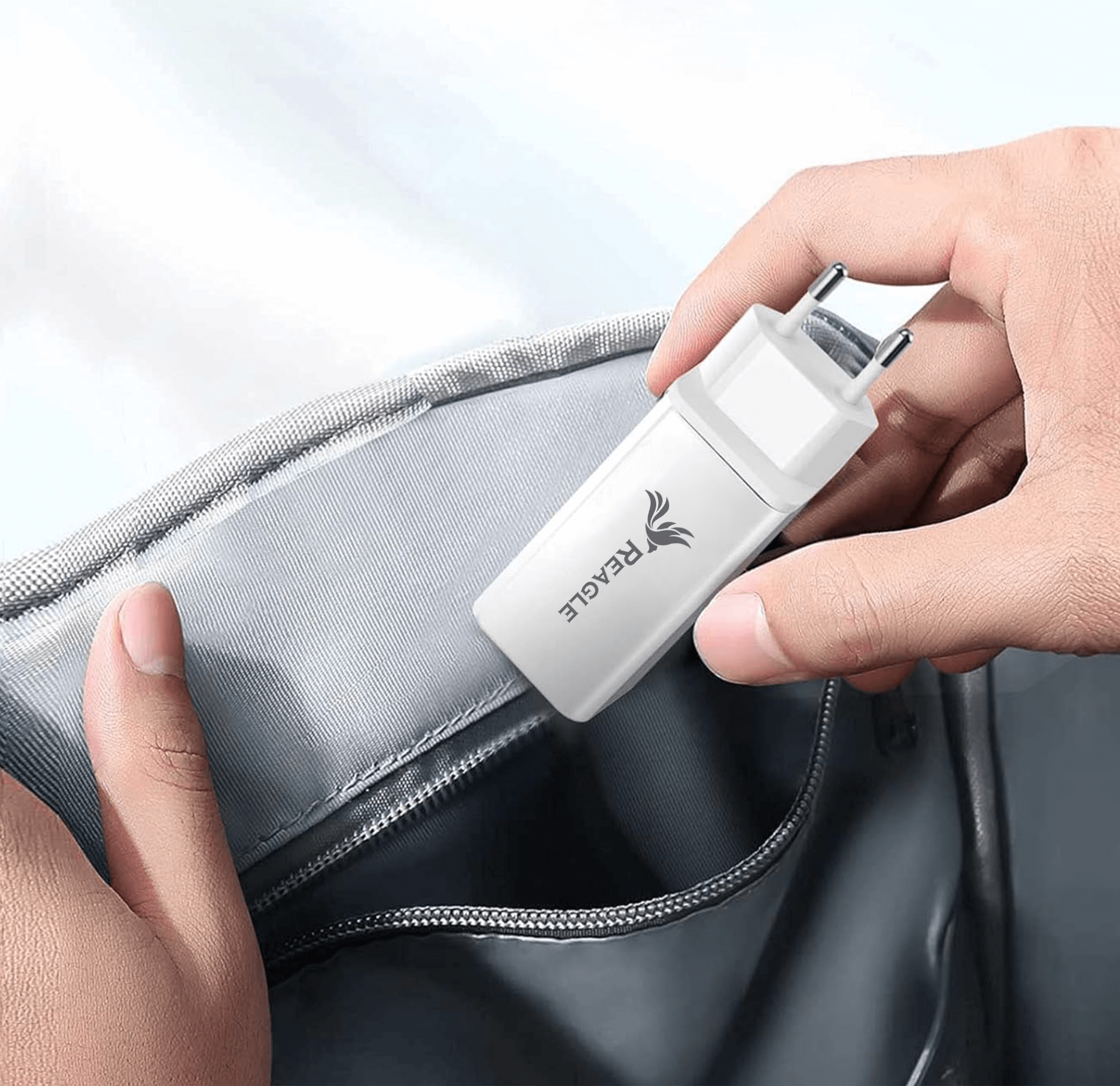 Ręka wkładająca białą ładowarkę do szarej kieszeni. Widoczne logo Reagle.