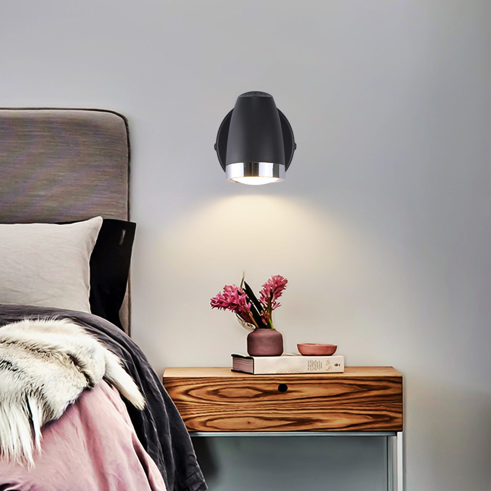 Czarny reflektor naścienny ze srebrnym pierścieniem, oświetlający stół z kwiatami.