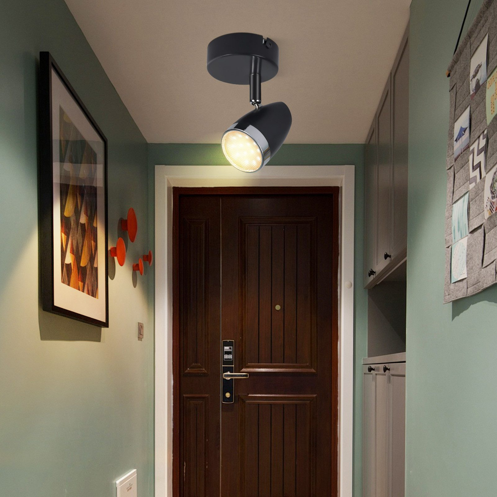 Korytarz z reflektorem, obrazem i dekoracją ścienną, z ciemnymi drzwiami.