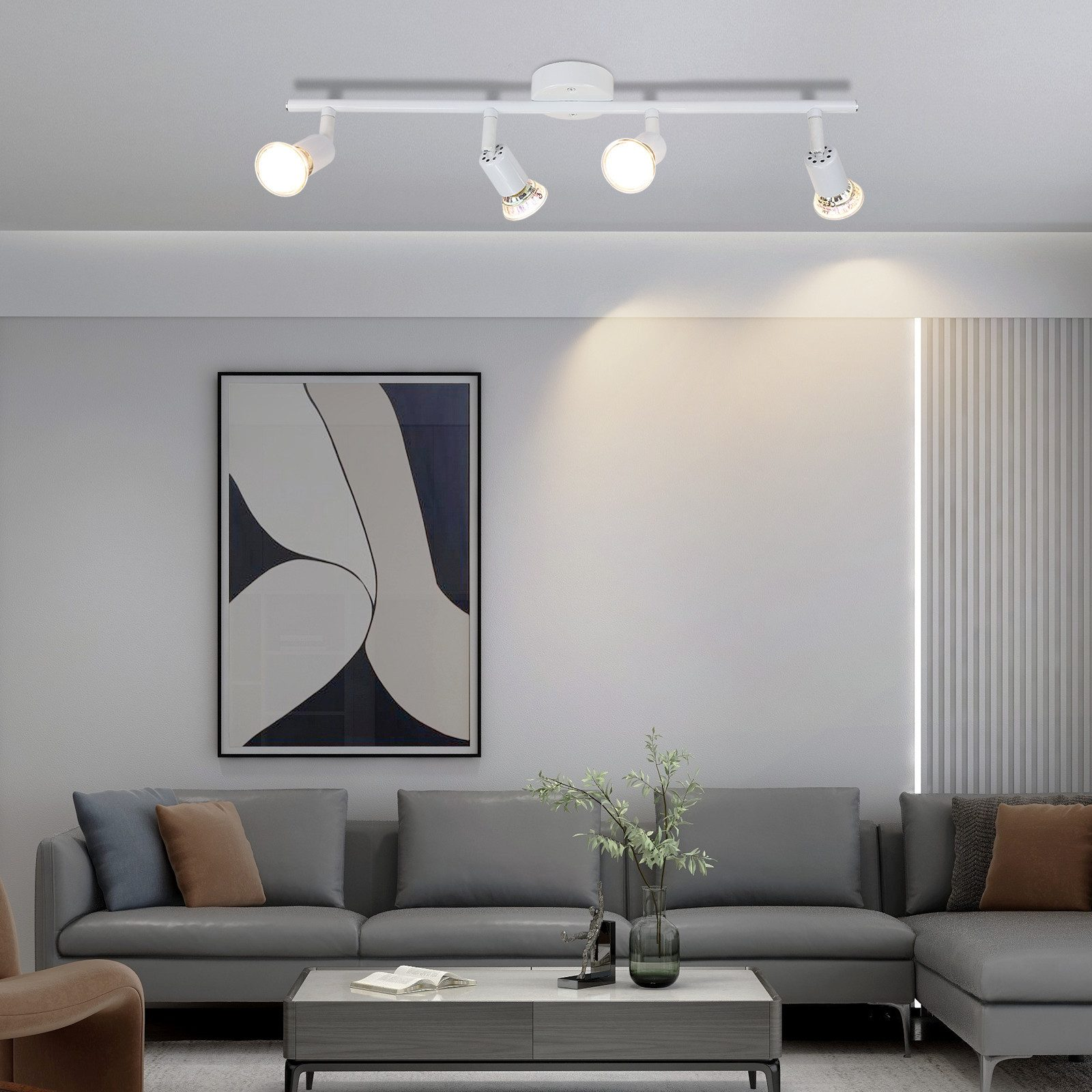 Salon z szarą sofą, stolikiem kawowym, obrazem i czterema reflektorami sufitowymi. Białe ściany i roślina.