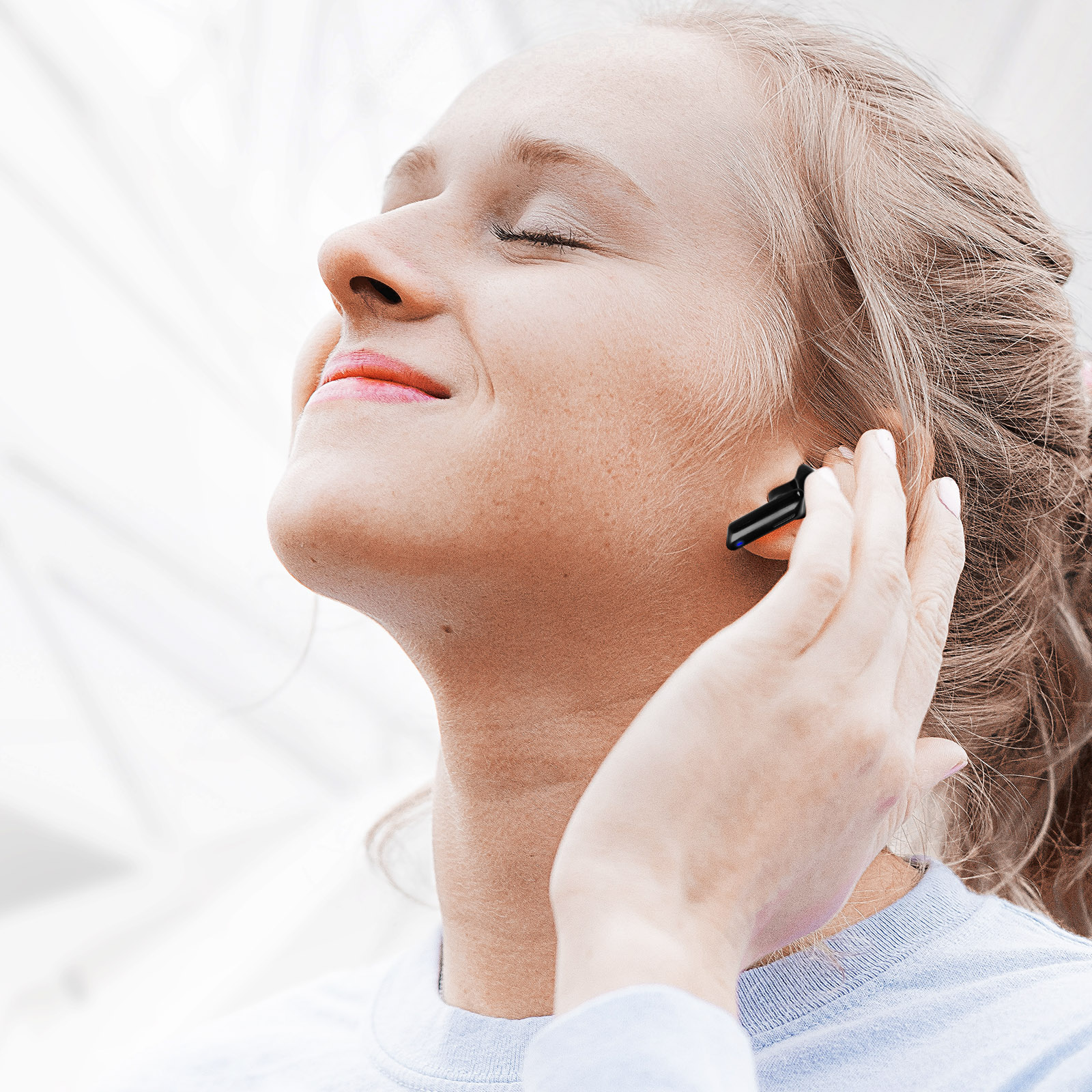 Une femme souriante portant une chemise bleue, un écouteur dans l'oreille, se touchant l'oreille.