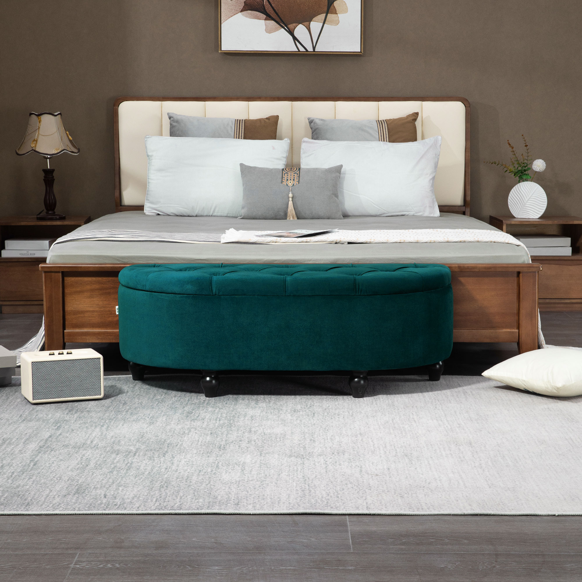 Schlafzimmer mit Bett und grünem Hocker. Das Bett hat Kissen und einen Holzrahmen. Auf dem Boden liegt ein Teppich.