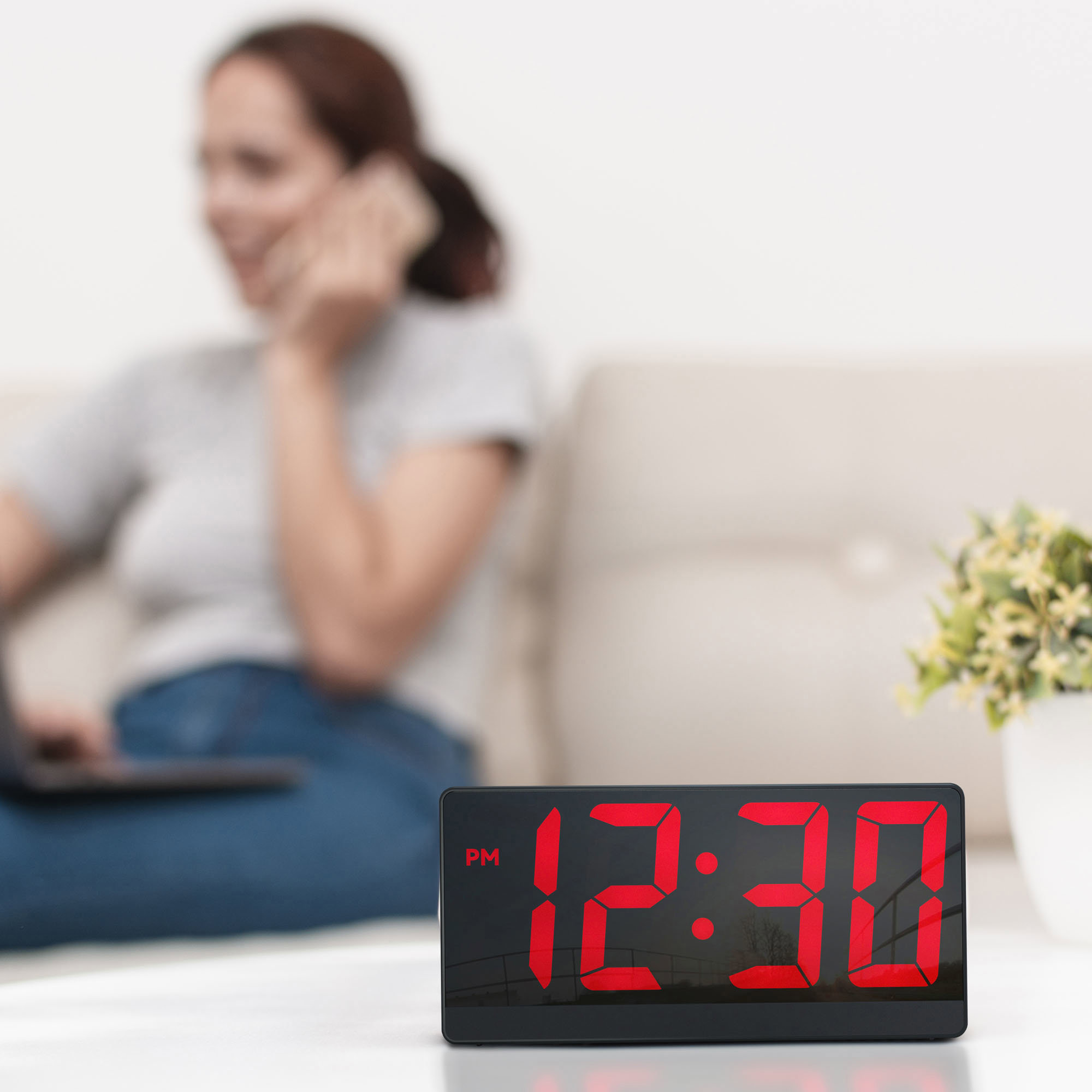 Digitaluhr mit 12:30 PM. Eine Frau unscharf im Hintergrund.