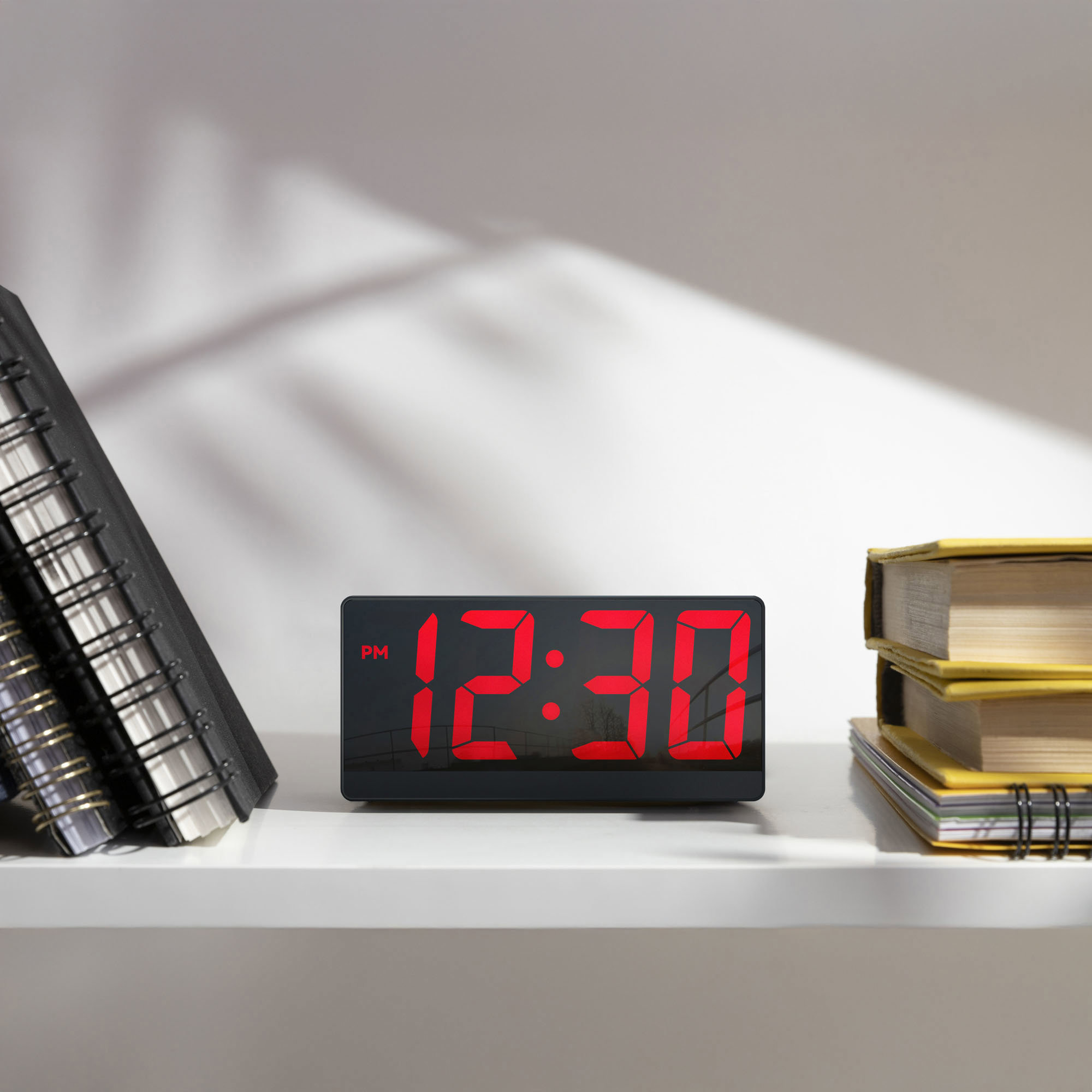Digitaluhr mit 12:30 PM auf einem weißen Regal. Bücher rechts.