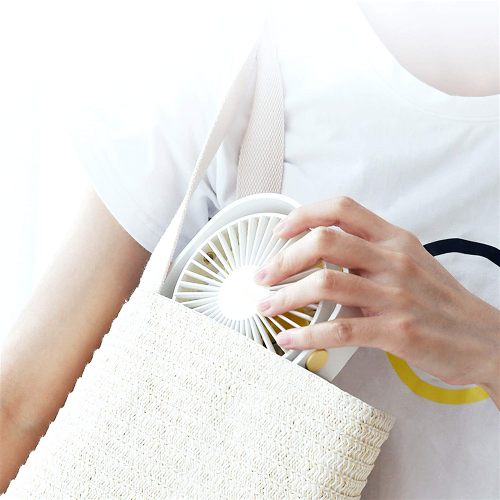 Hand einer Person, die einen weißen tragbaren Ventilator in einer weißen gewebten Tasche hält. Weißes Hemd.
