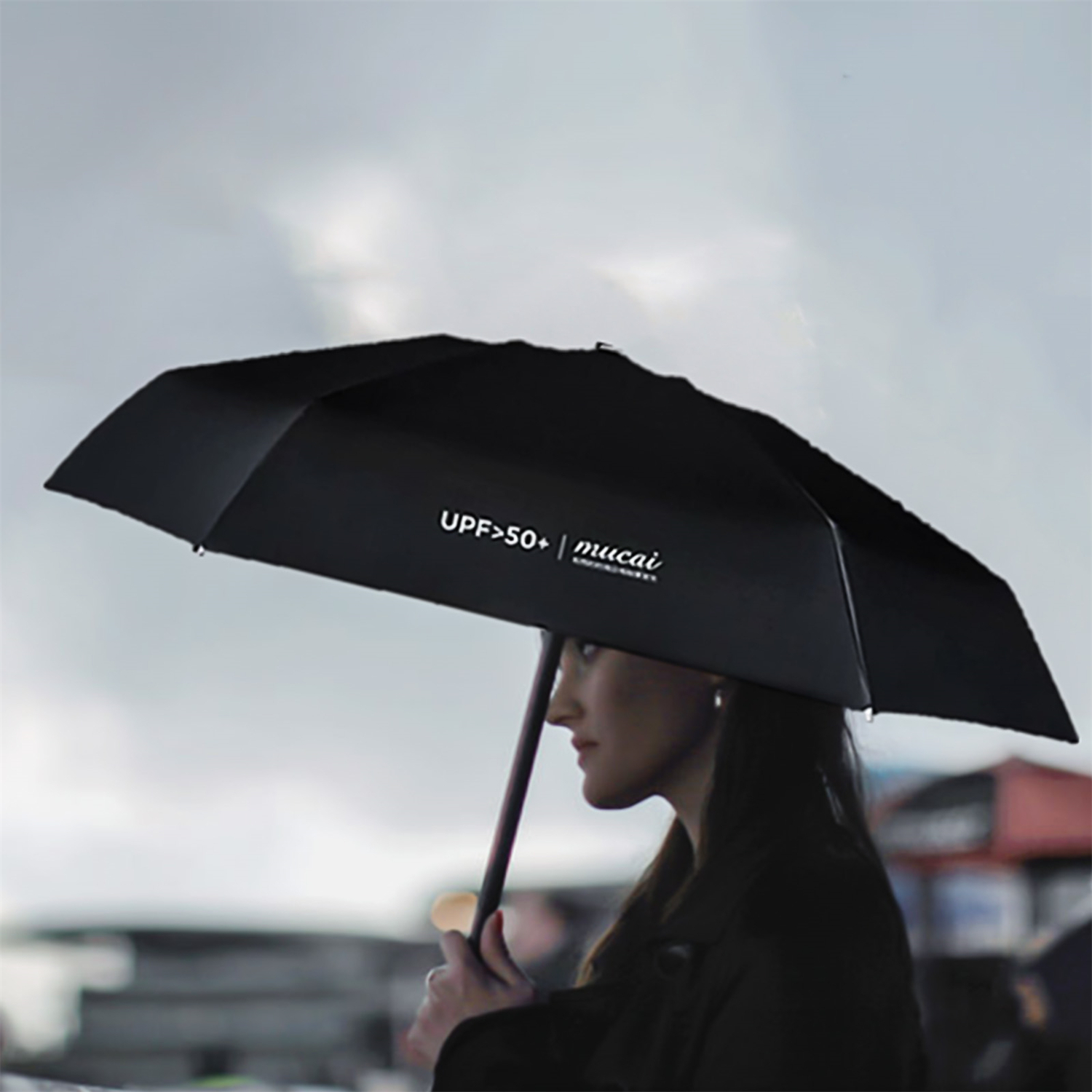 Frau hält schwarzen Regenschirm mit weißem Text. Wolkenhimmel im Hintergrund.