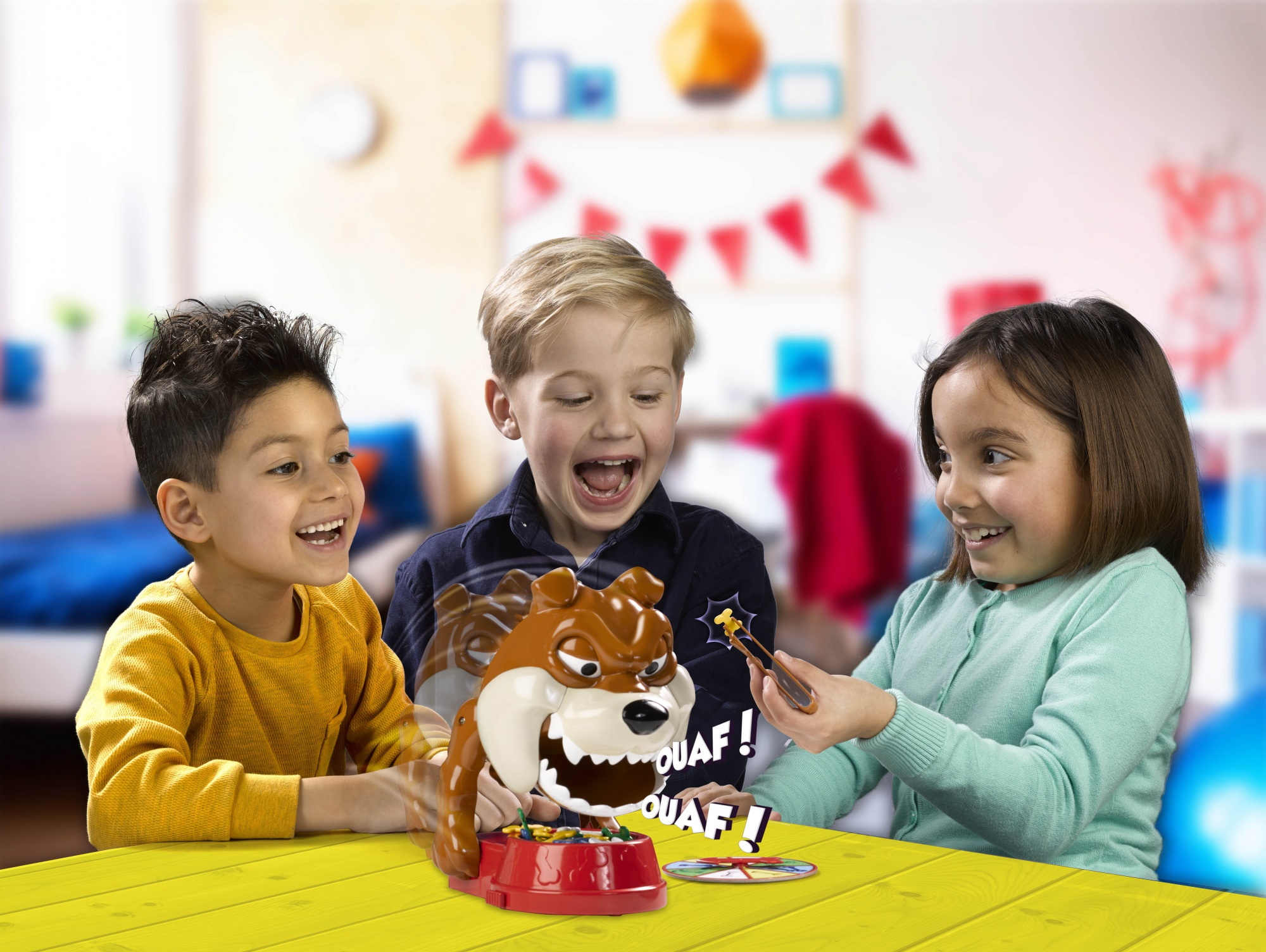 Tre bambini giocano con una testa di bulldog. Tavolo giallo. Sfondo bianco.