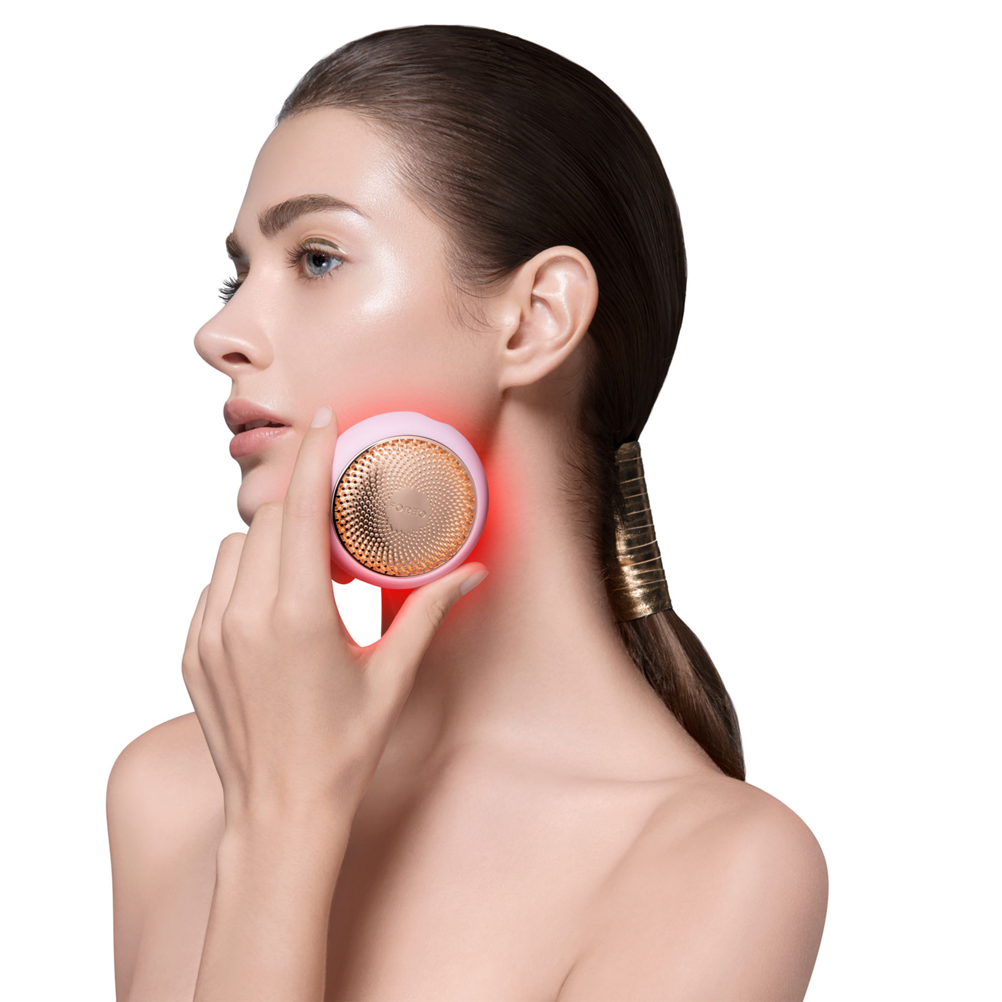Mujer sostiene un dispositivo facial rosa en su mejilla. El dispositivo tiene una luz roja.
