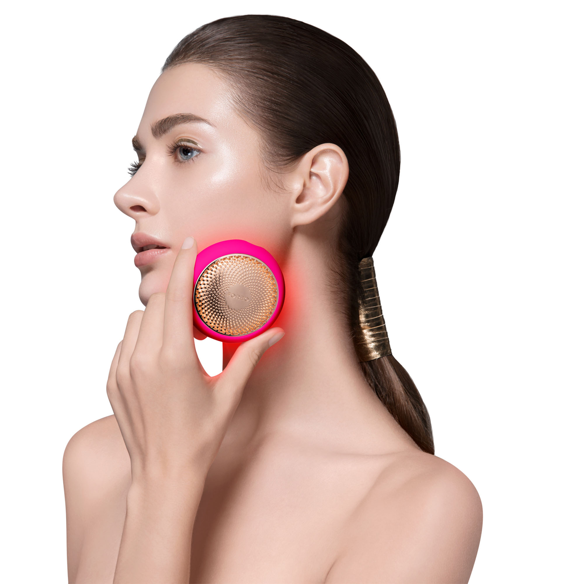 Mujer sosteniendo un dispositivo de limpieza facial rojo y rosa en su rostro.