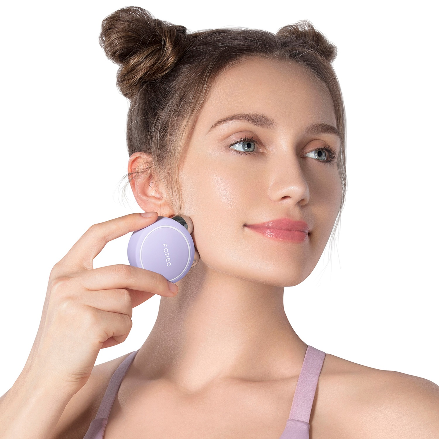 Una donna usa un dispositivo FOREO lilla sul suo viso. Sfondo bianco.