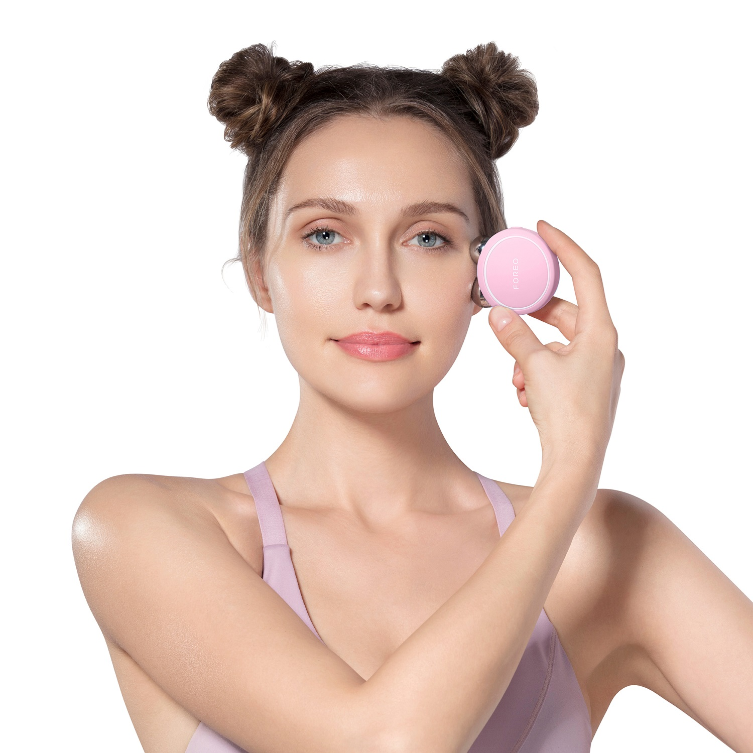 Una donna tiene in mano un massaggiatore facciale rosa, con i capelli raccolti in chignon, su sfondo bianco.