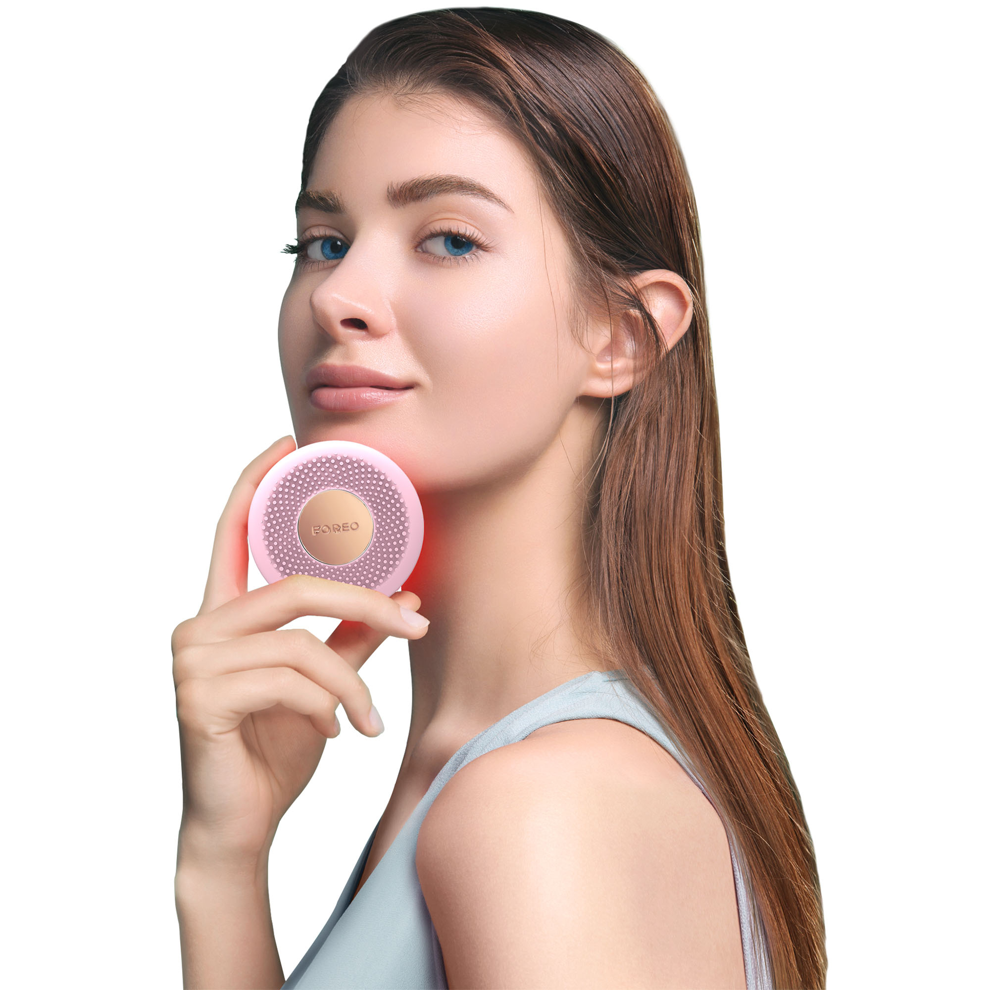 Una donna tiene un dispositivo Foreo rosa vicino al viso, con luce rossa visibile.