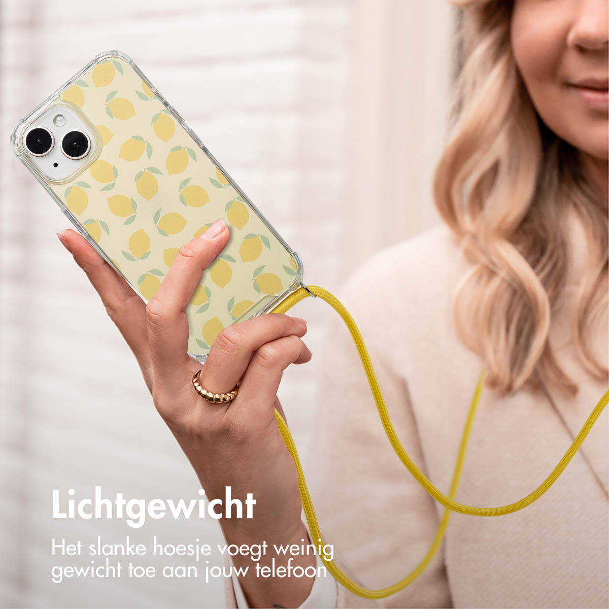 Vrouw houdt telefoon vast met citroenhoesje en lanyard. Gele lanyard, gouden ring om de vinger.