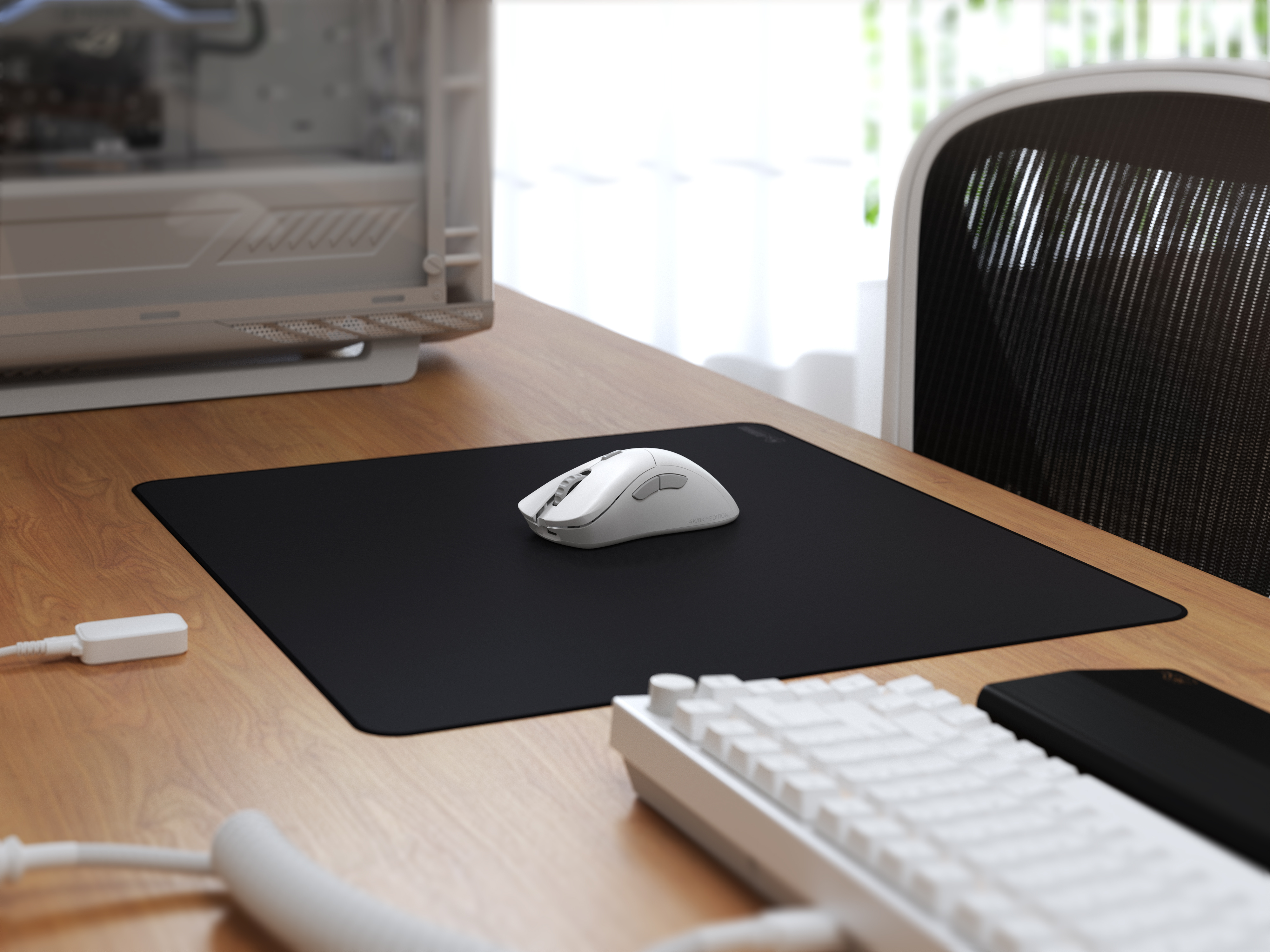 Biała mysz na czarnej podkładce, klawiatura i obudowa komputera na drewnianym biurku.