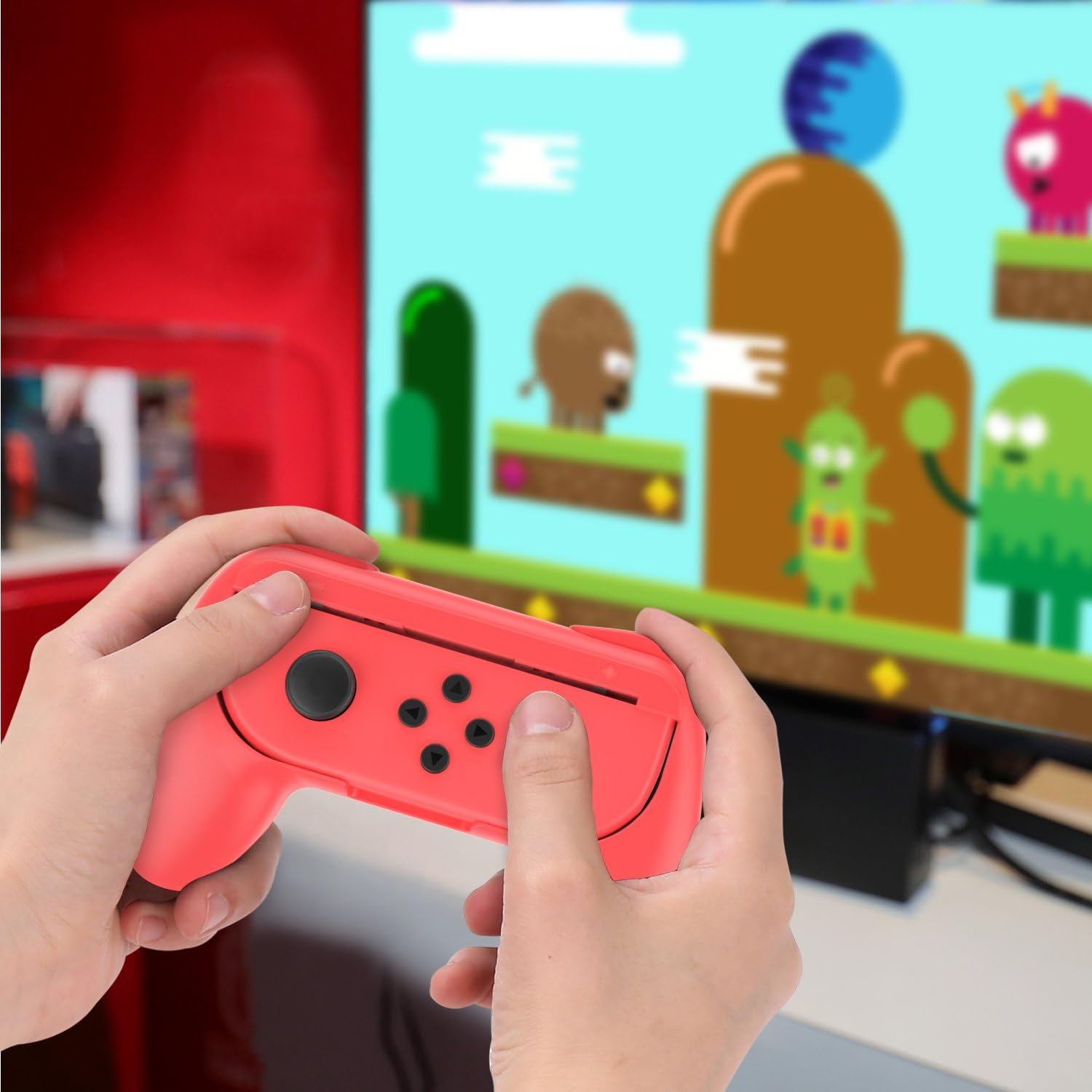 Hände halten einen roten Spielcontroller und spielen ein Spiel auf einem Bildschirm mit Cartoonfiguren.