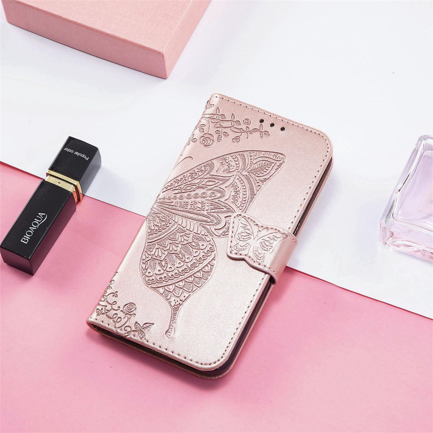 Funda rosa para teléfono con diseño de mariposa, junto a perfume y labial.