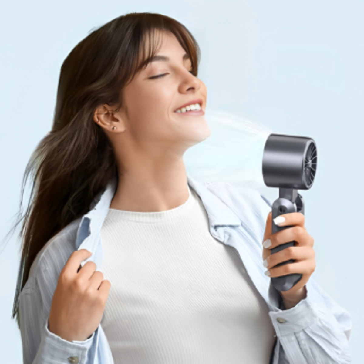 Lächelnde Frau hält einen grauen Ventilator, Luft bläst in ihr Gesicht.