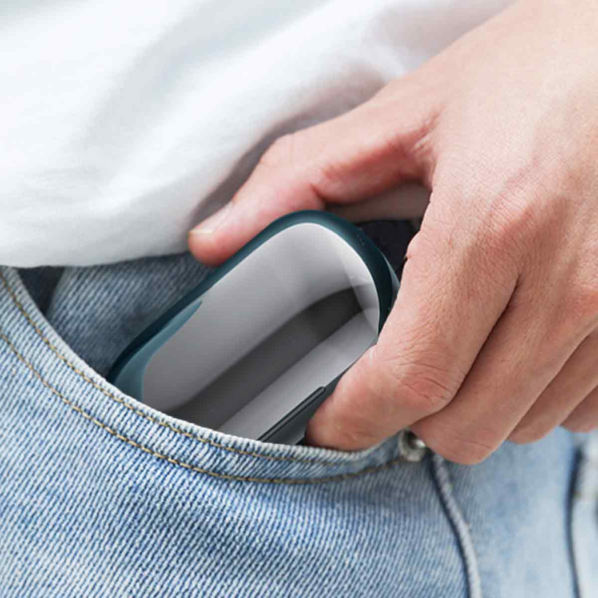 Eine Hand steckt ein kleines, weiß-graues Gerät in eine Jeanstasche.