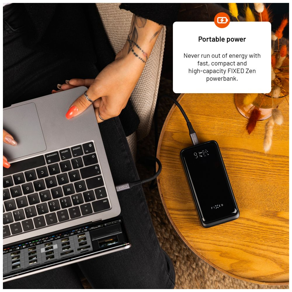 Eine Person, die einen Laptop verwendet, der an eine Powerbank angeschlossen ist. Die Powerbank ist schwarz und trägt die Aufschrift 'FIXED'.