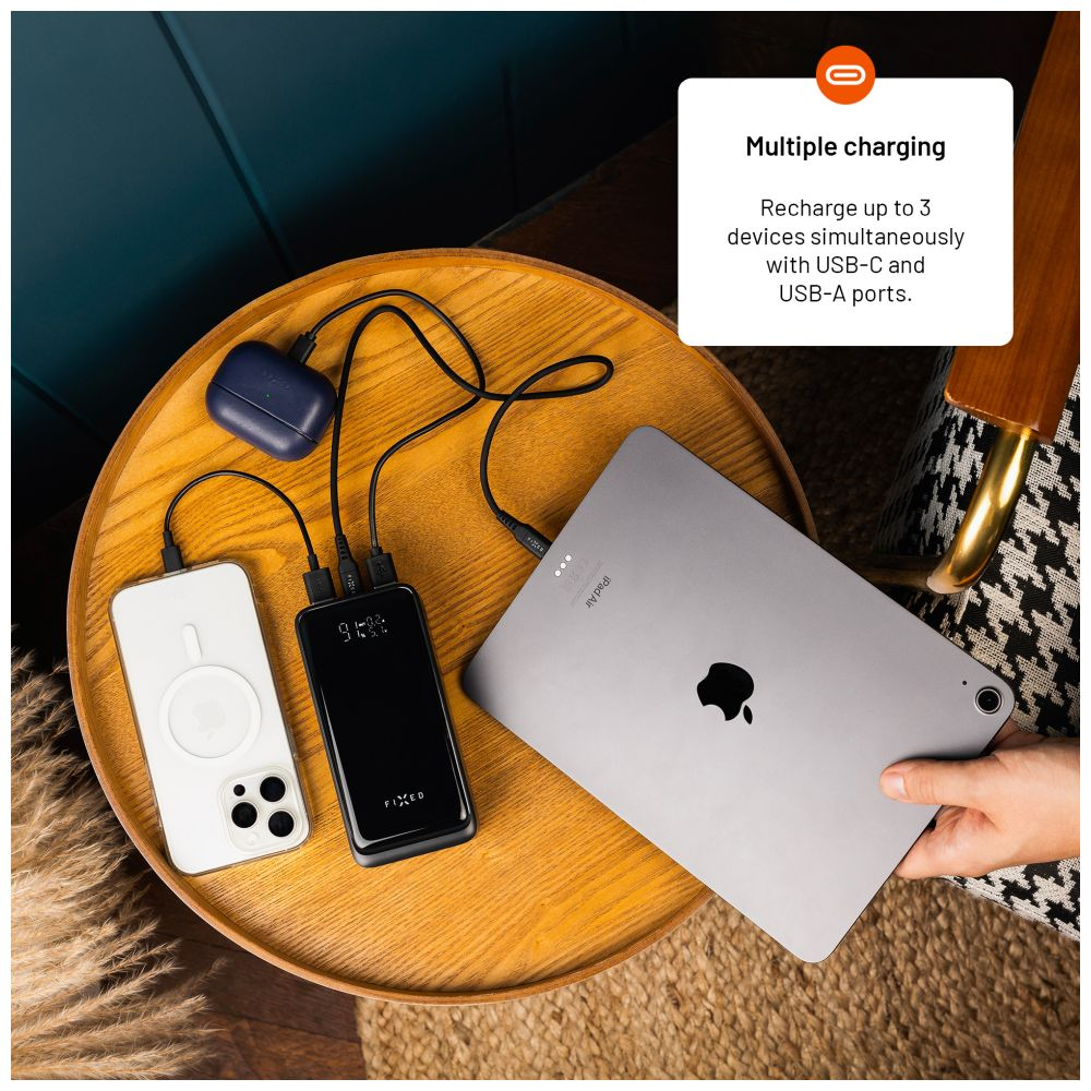 Eine Person benutzt eine Powerbank, um ein Telefon, ein Tablet und Ohrhörer aufzuladen. Die Powerbank ist schwarz.
