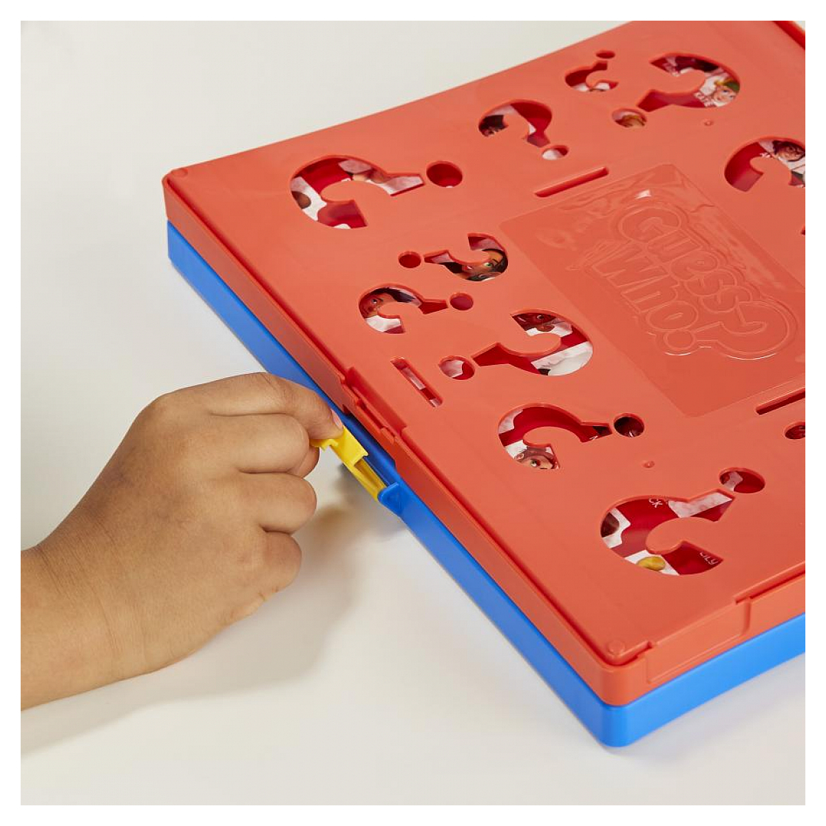 Een hand opent een Guess Who bordspel. Het bord is rood en blauw, met vraagtekens.