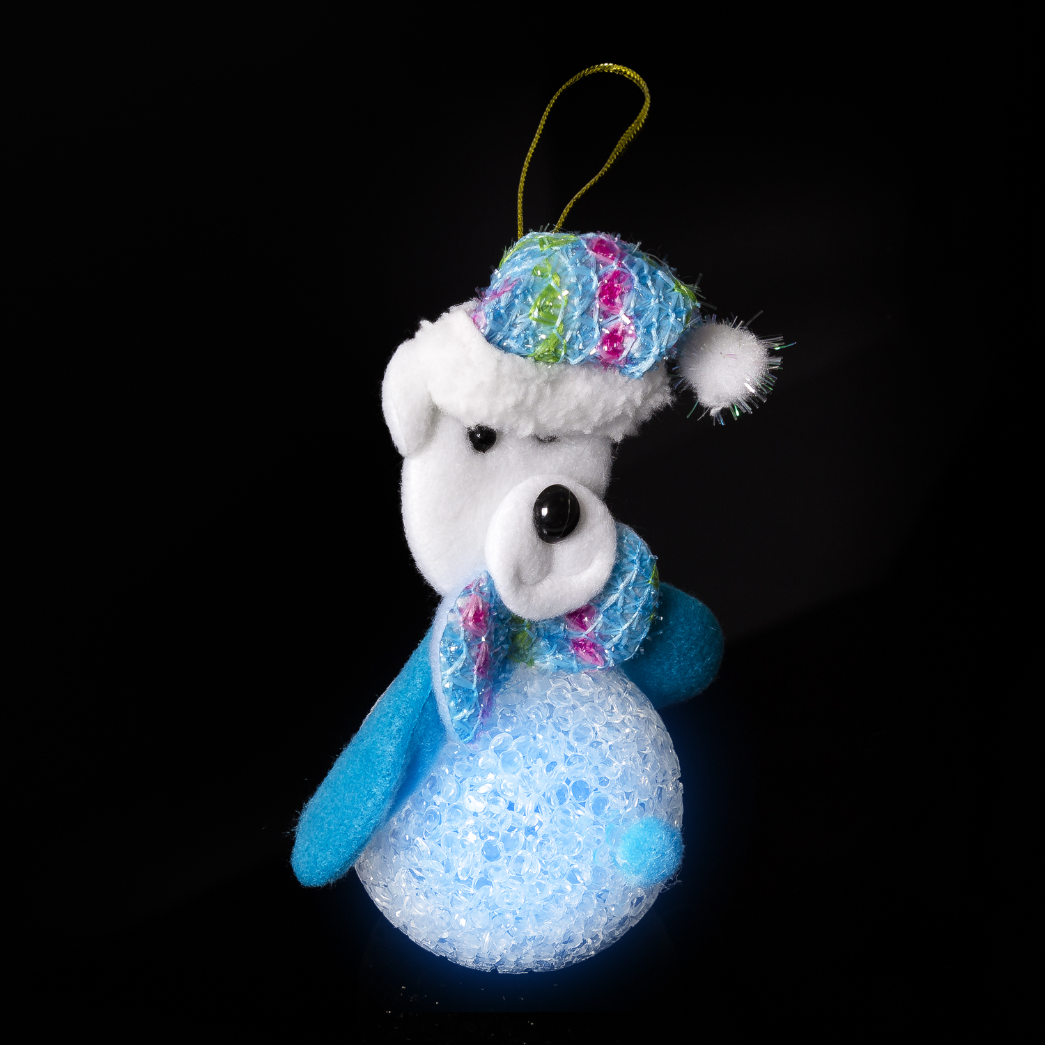 Ornamento natalizio a forma di orso polare di peluche bianco con cappello e sciarpa blu su sfondo nero.