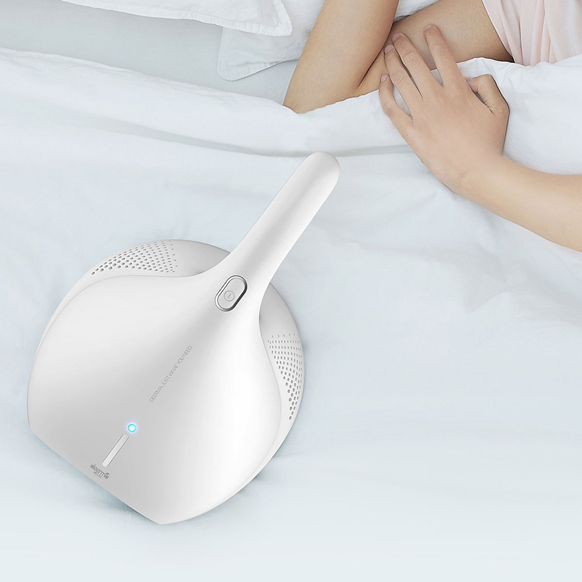 Biały odkurzacz na łóżku, widoczna ręka i noga osoby.