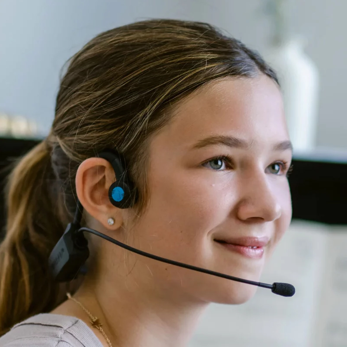 Ein Mädchen mit einem blau-schwarzen Headset lächelt. Ein Mikrofon erstreckt sich vom Headset.