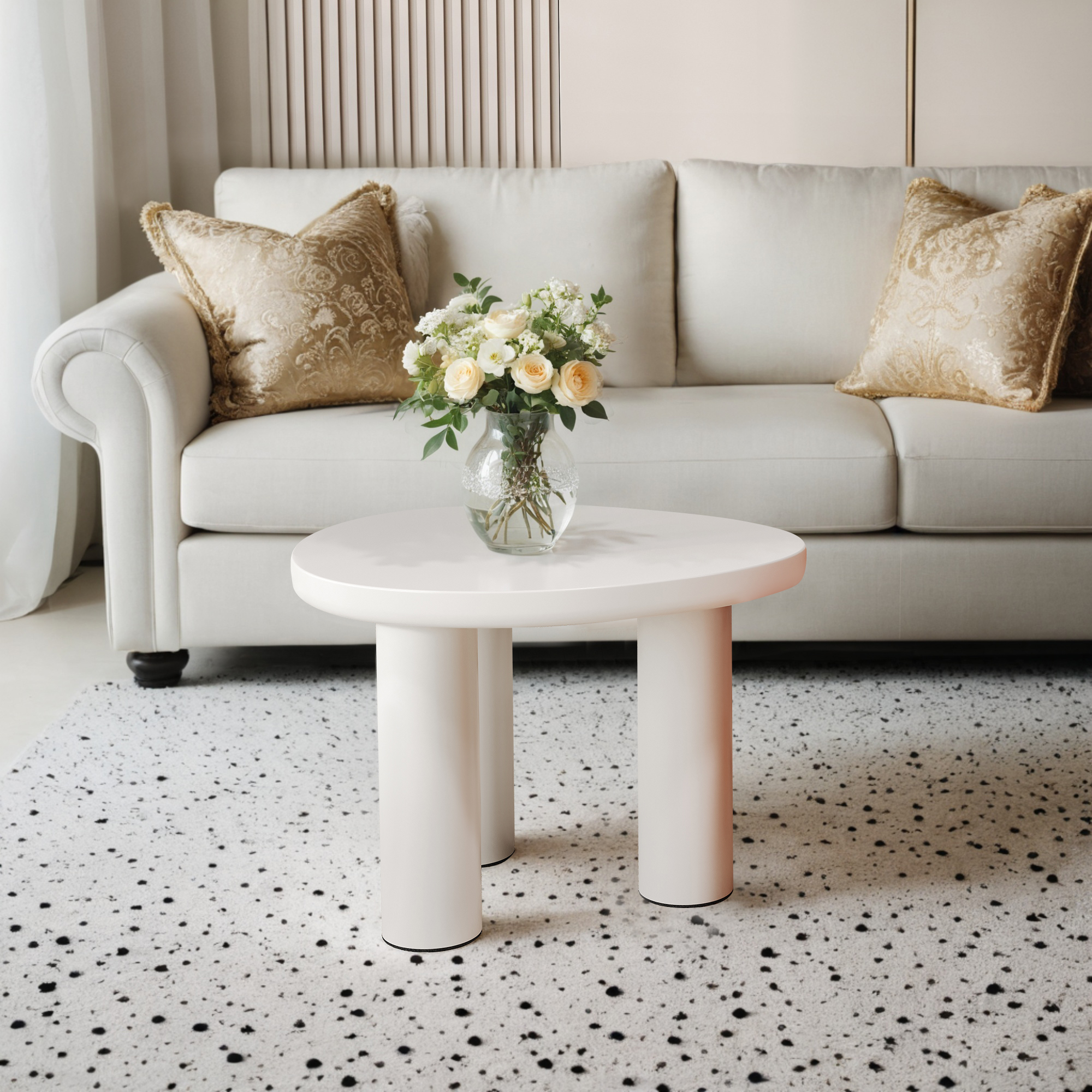 Weißer runder Tisch mit Blumen und Sofa. Beige Couch mit goldenen Kissen.