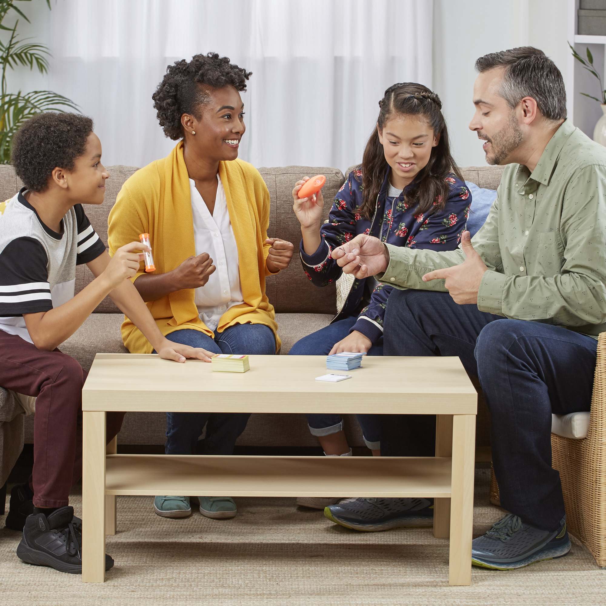 Familie die een spel speelt. Tafel met kaarten, timer en zoemer. Mensen lachen en interageren.