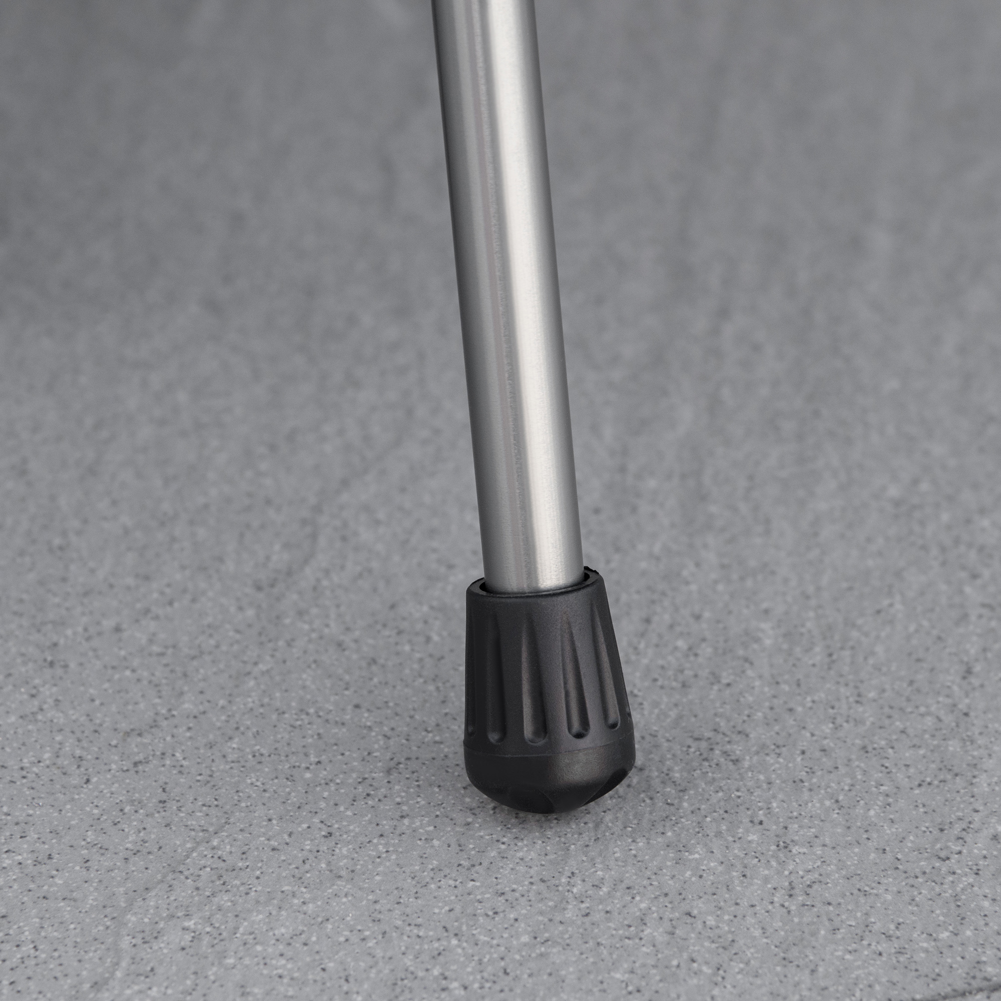 Nahaufnahme eines Bettbeins. Silbernes Metall mit einem schwarzen Gummifuß. Grauer Boden.