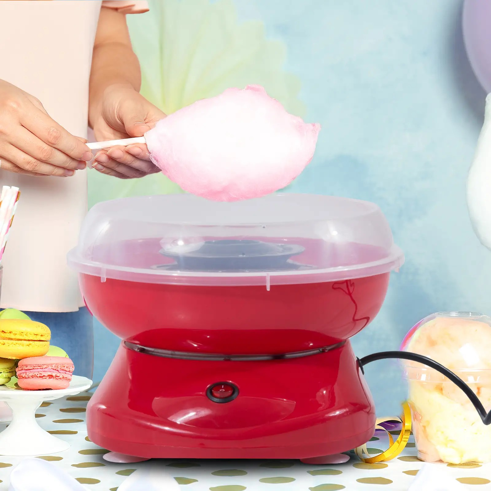 Person, die Zuckerwatte mit einer roten Maschine, rosa Zuckerwatte und Makronen herstellt.