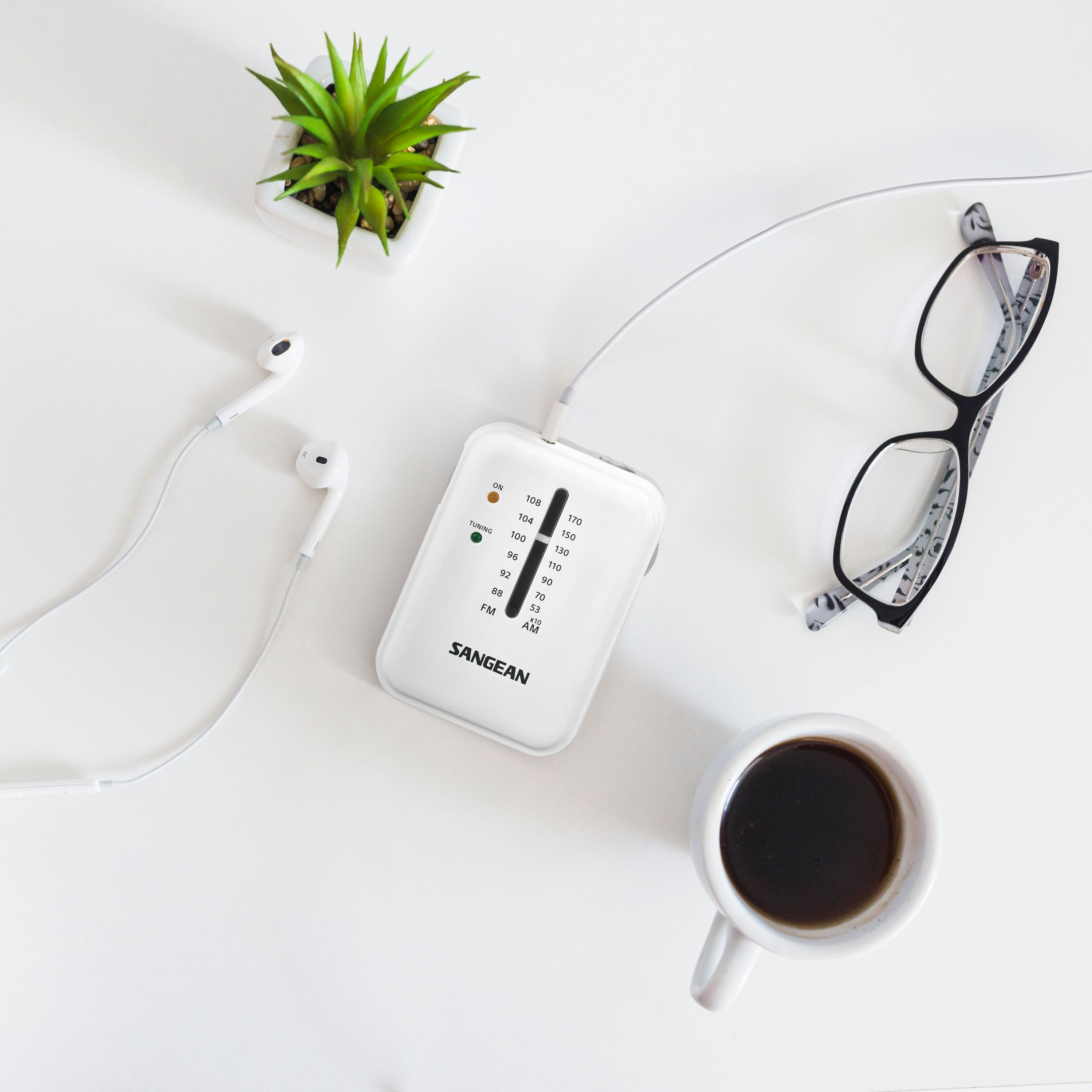 Widok z góry na radio, słuchawki, kawę, okulary i roślinę.