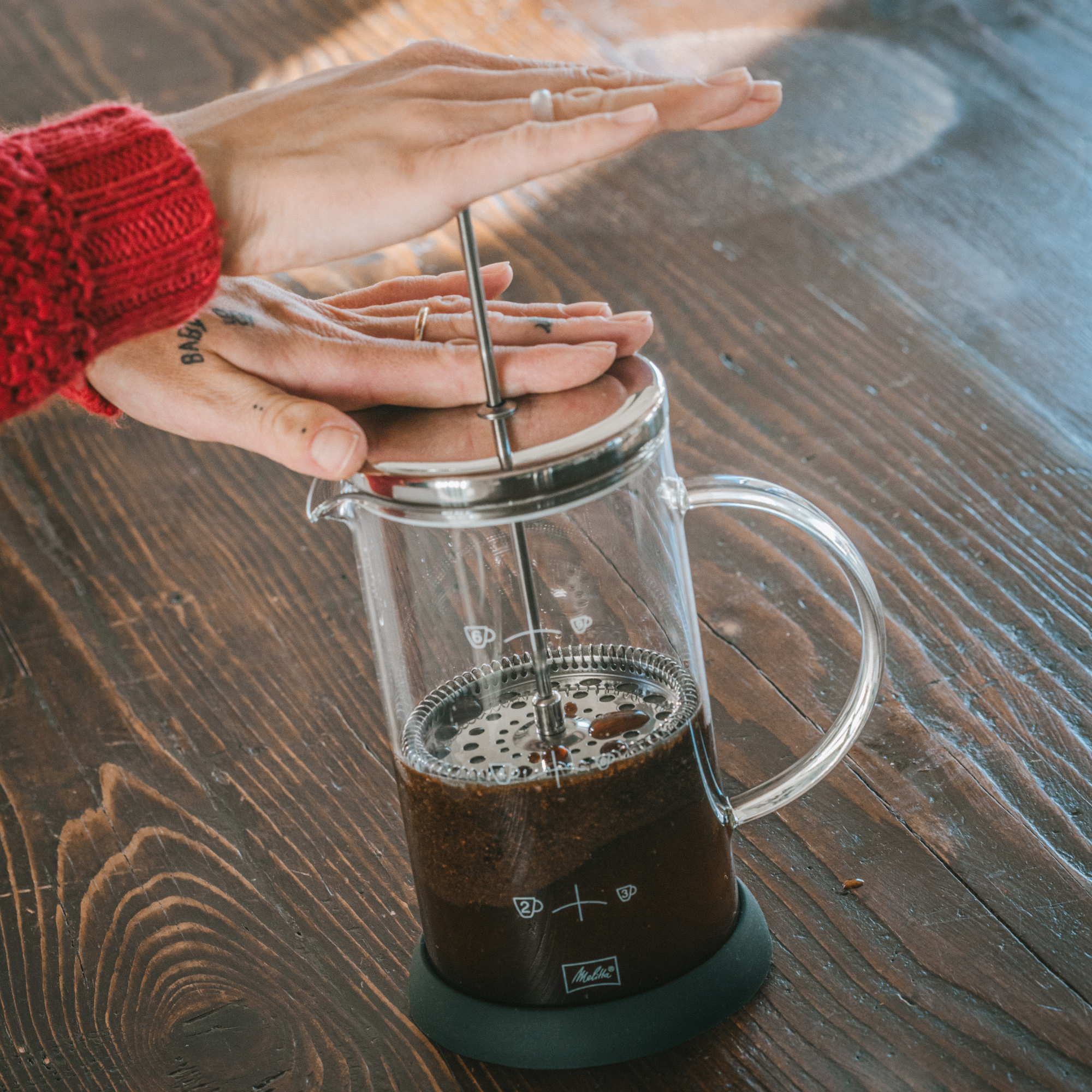 Una mano che preme una pressa per caffè. Caffè nella pressa. Tavolo di legno. Primo piano.