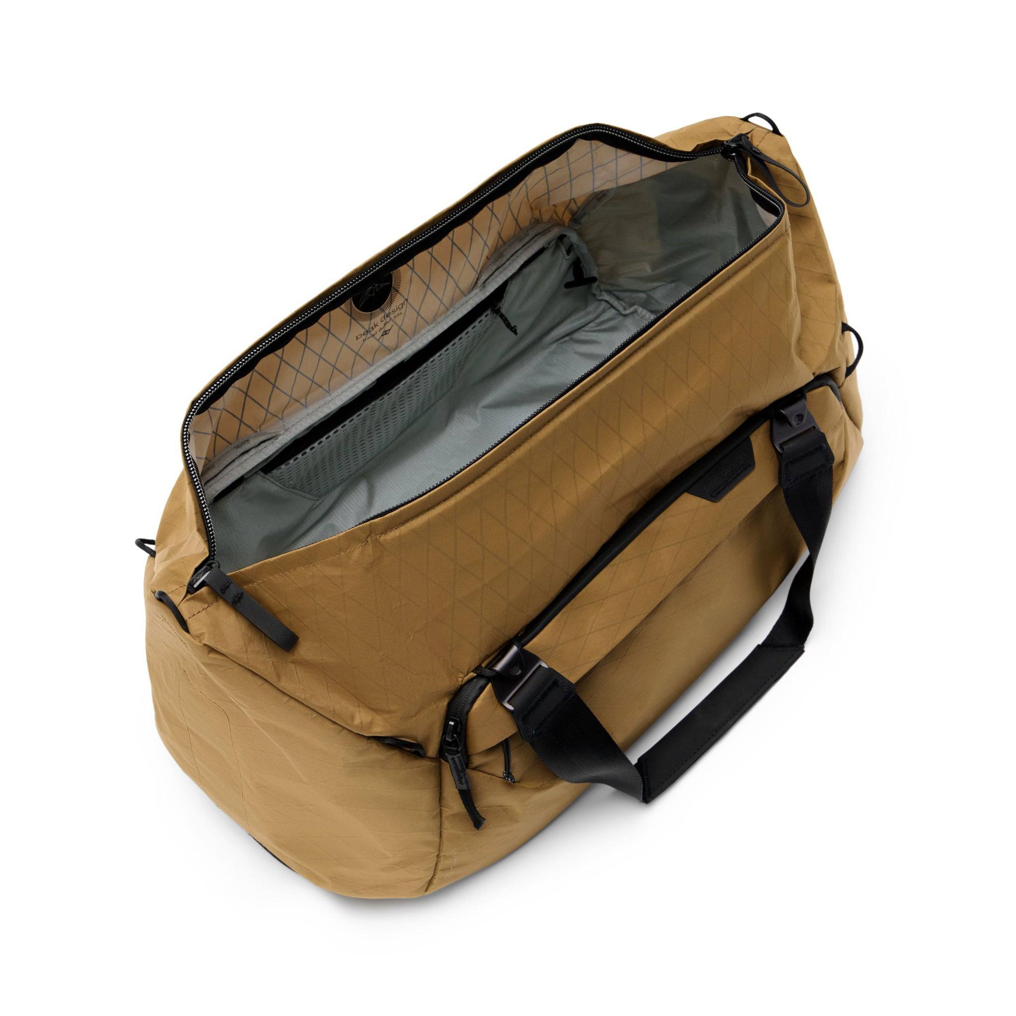 Jasnobrązowa torba podróżna, otwarta, pokazująca wnętrze. Torba ma czarne paski i zamki błyskawiczne.