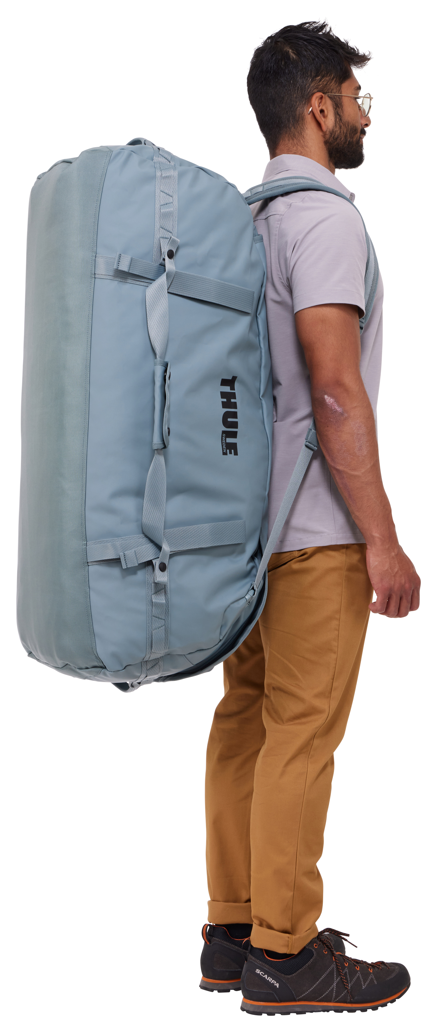Mann mit Brille trägt eine große blaue Thule-Reisetasche auf dem Rücken.
