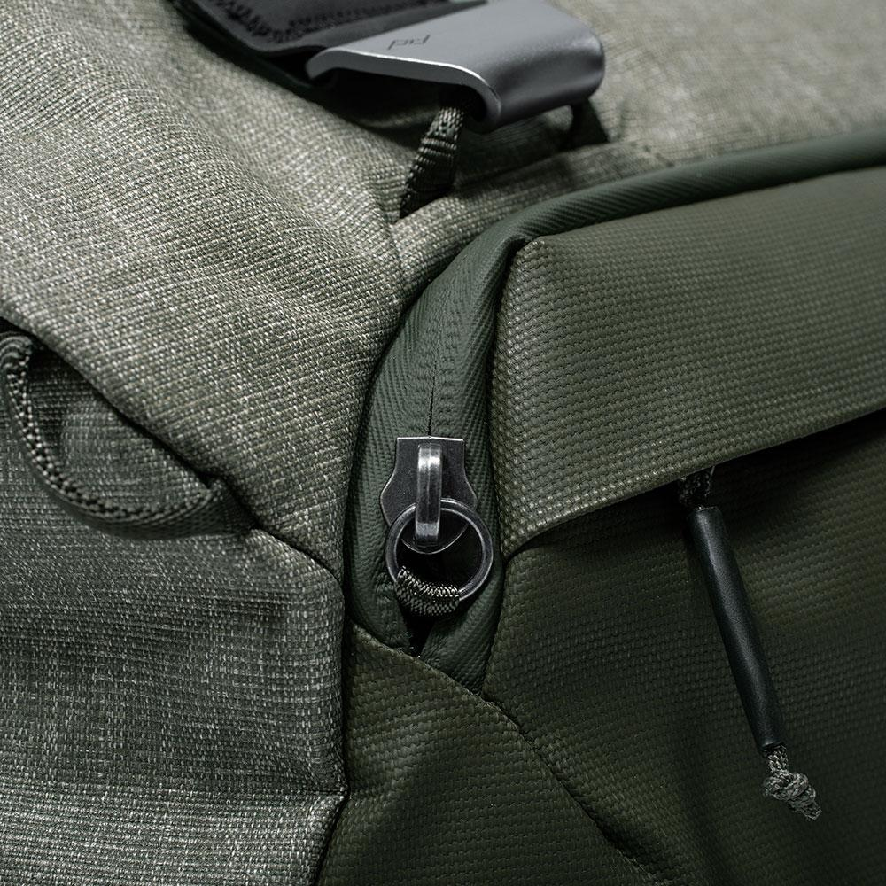 Nahaufnahme eines grünen und grauen Rucksacks mit Reißverschluss und silberner Metallschnalle.