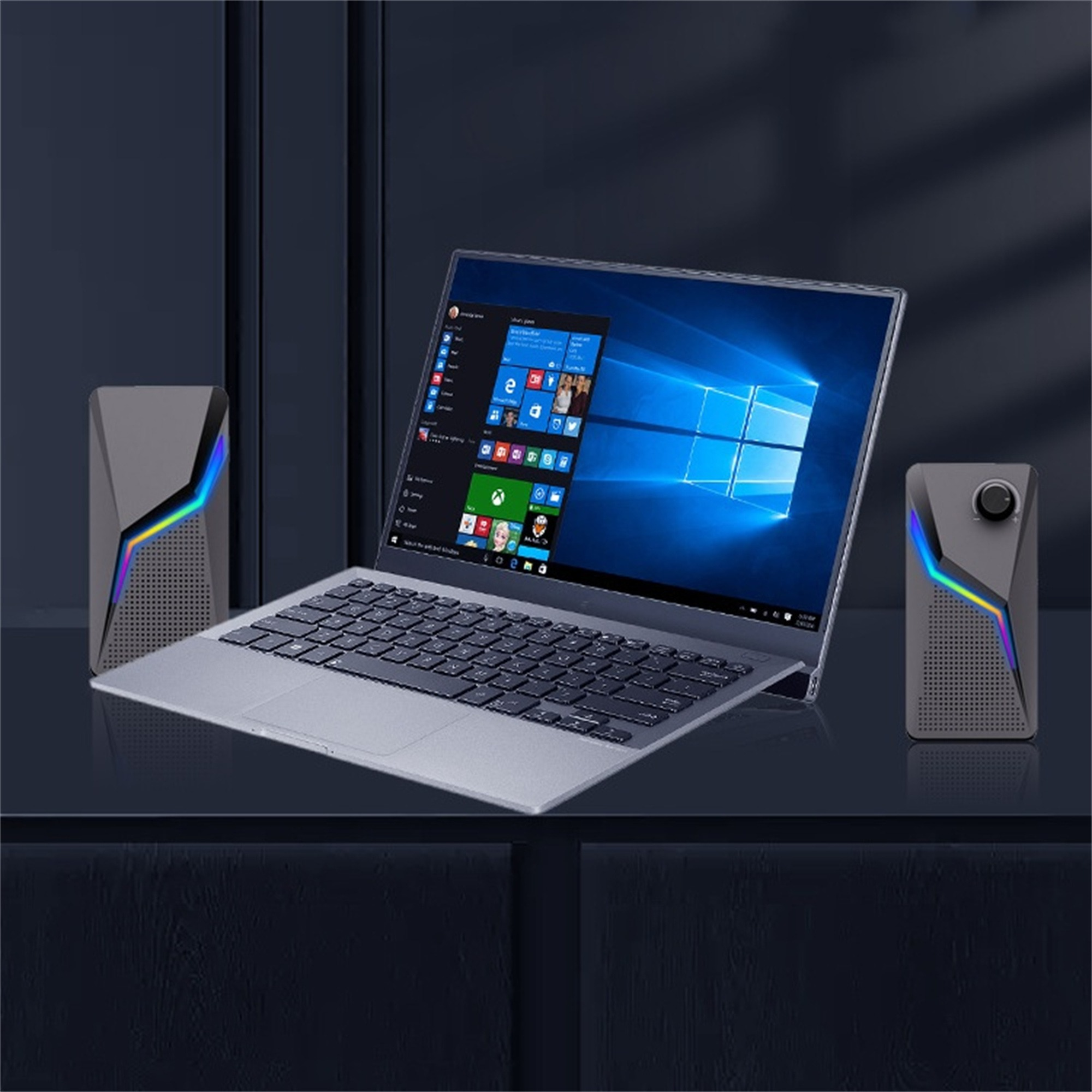 Ein Laptop und zwei Lautsprecher mit bunten Lichtern auf einer dunklen Oberfläche.