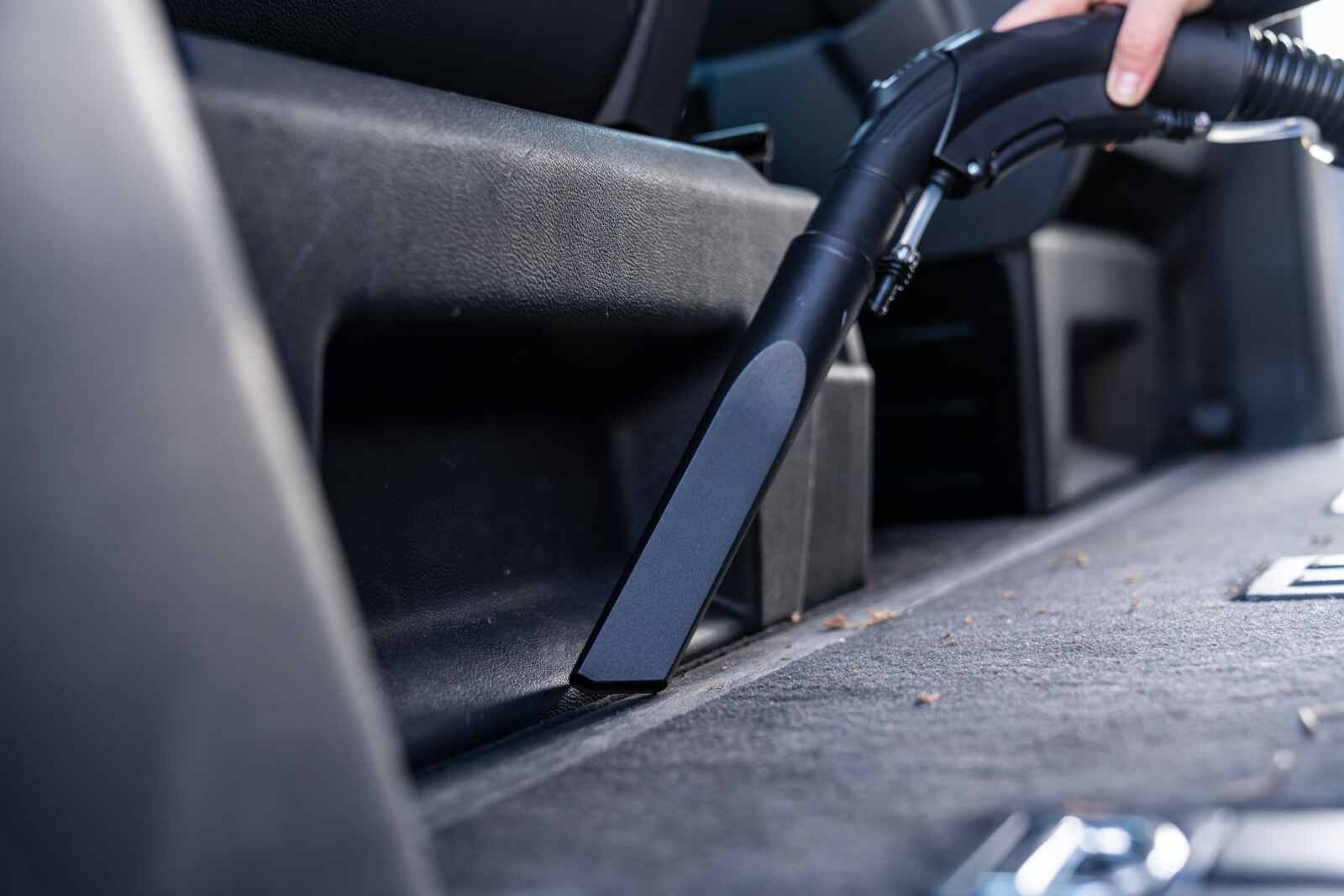 Stofzuiger mondstuk reinigt de binnenkant van een auto, verwijdert vuil. Hand houdt het mondstuk vast. De stoel is zichtbaar.