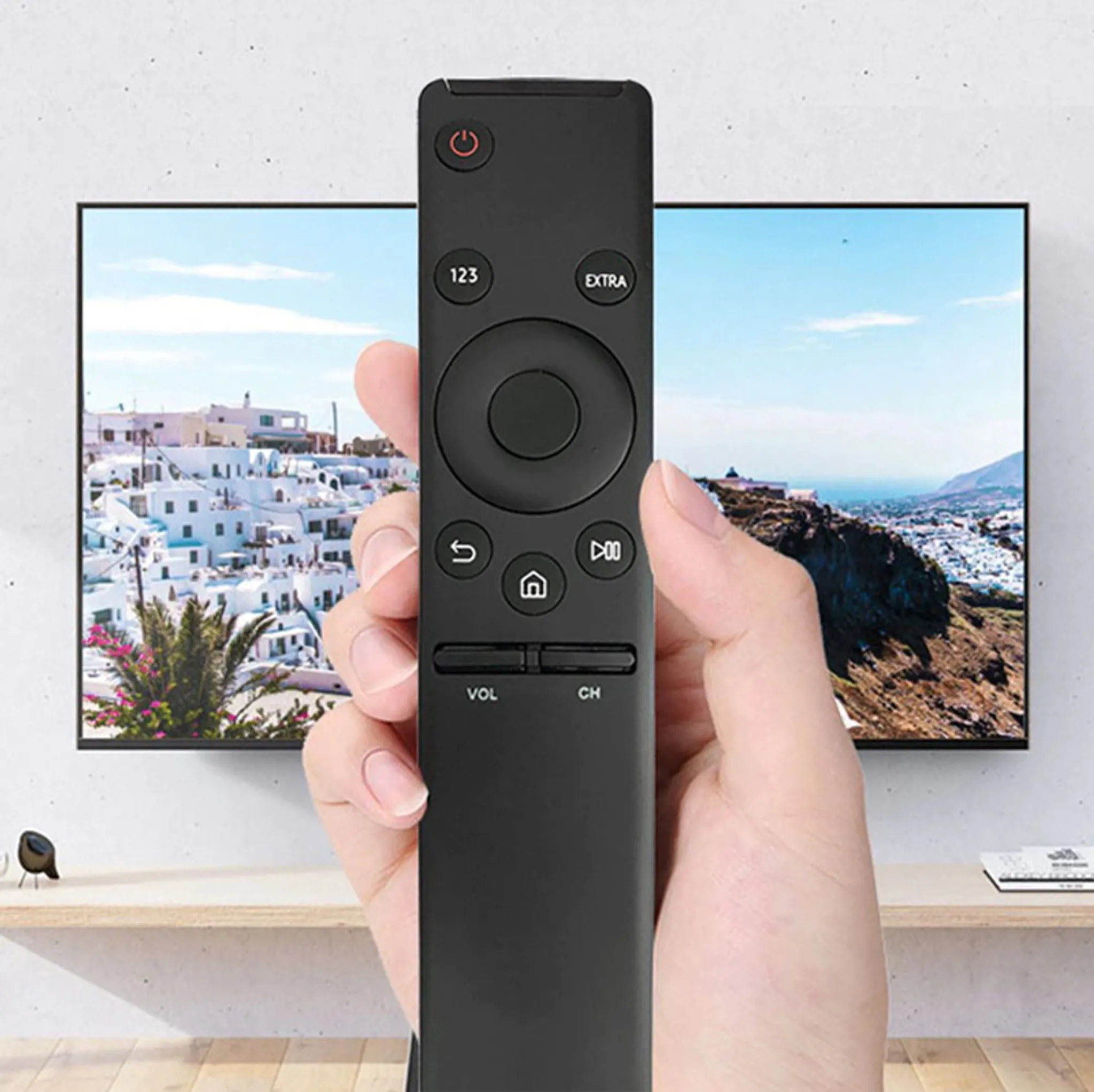 Hand, die eine schwarze Fernbedienung vor einem Fernseher hält, der eine Landschaft zeigt.
