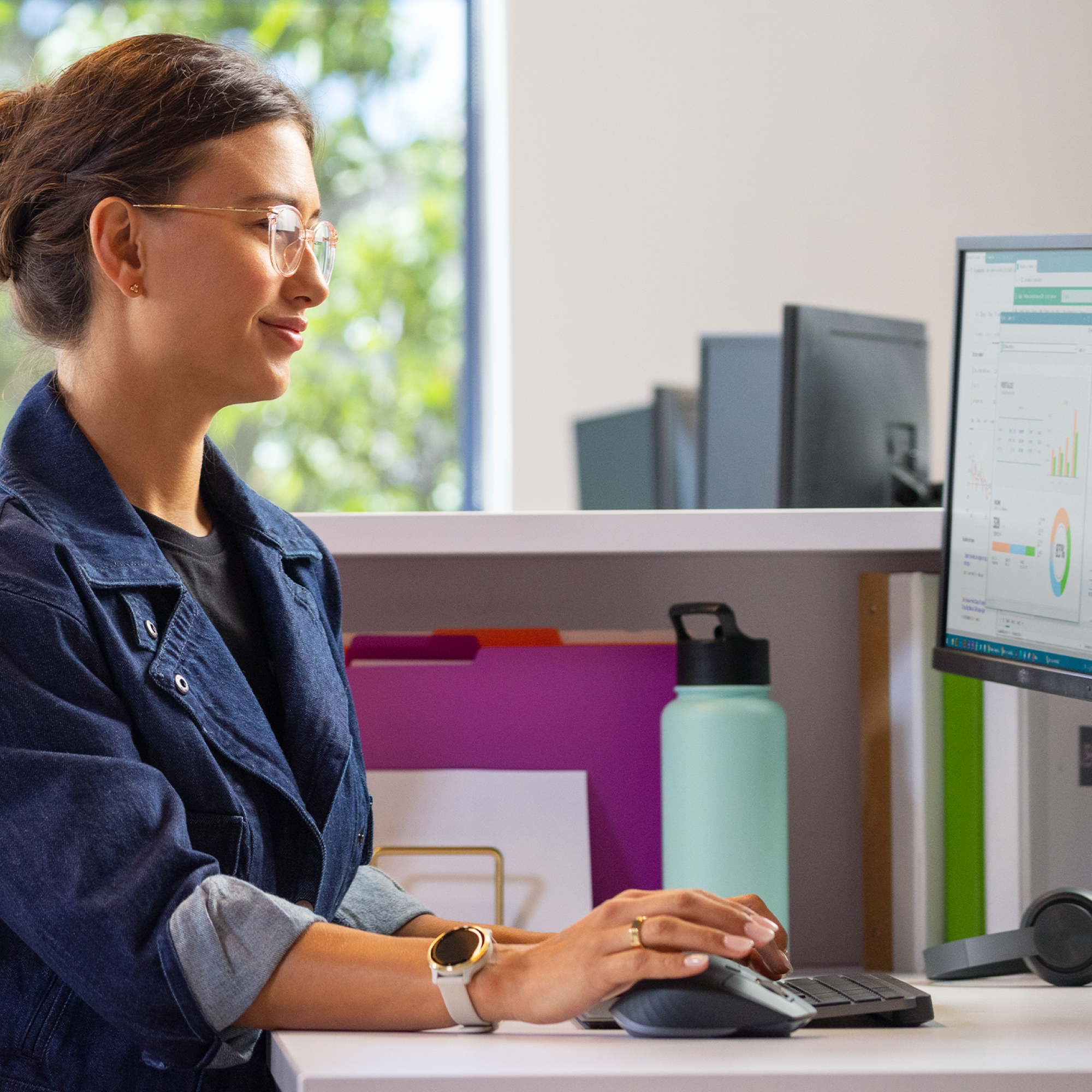 Donna che lavora al computer con mouse e tastiera. Una bottiglia d'acqua è sulla scrivania.