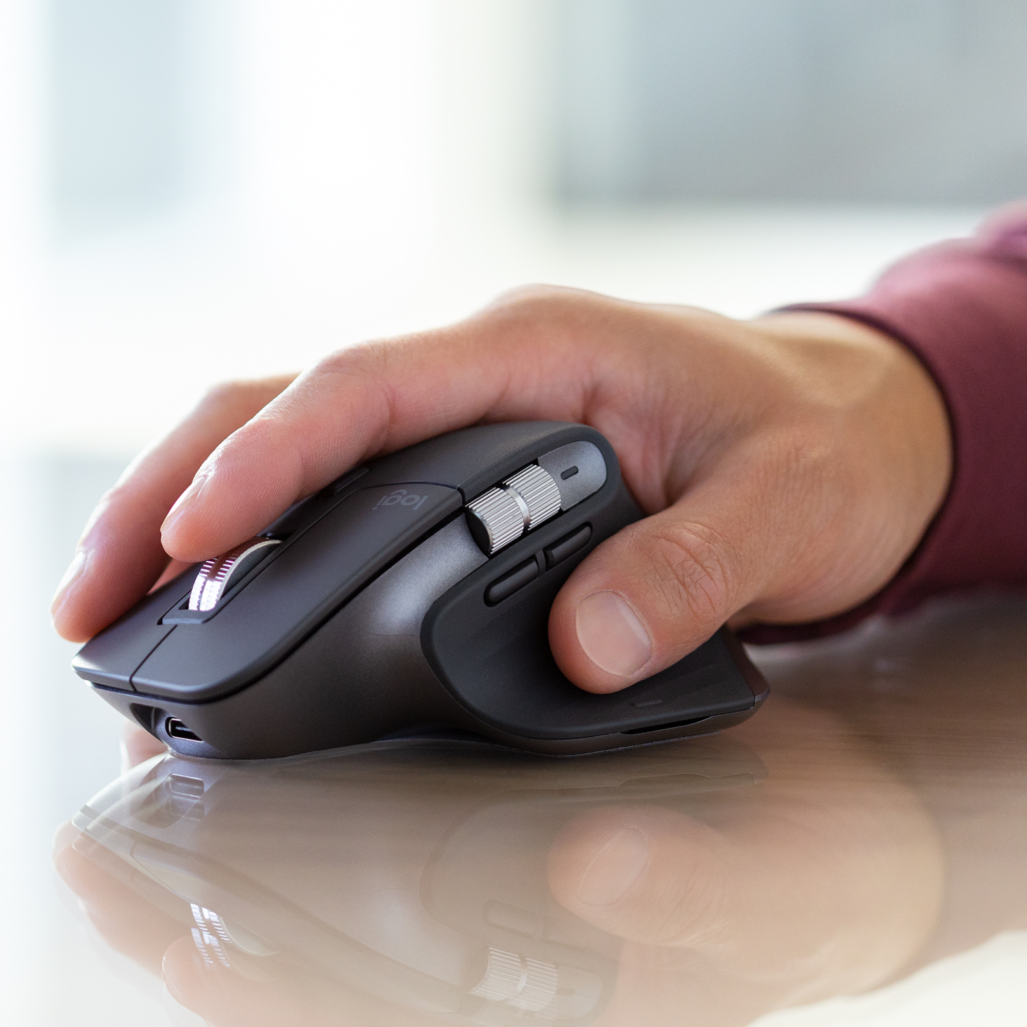 Mano che tiene un mouse nero. Il mouse è su una superficie riflettente. Lo sfondo è sfocato.