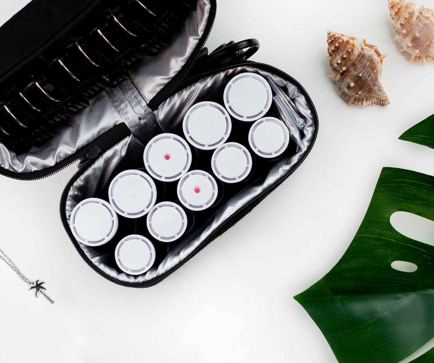 Open black case with hair curlers, shells, and leaf on white background.
