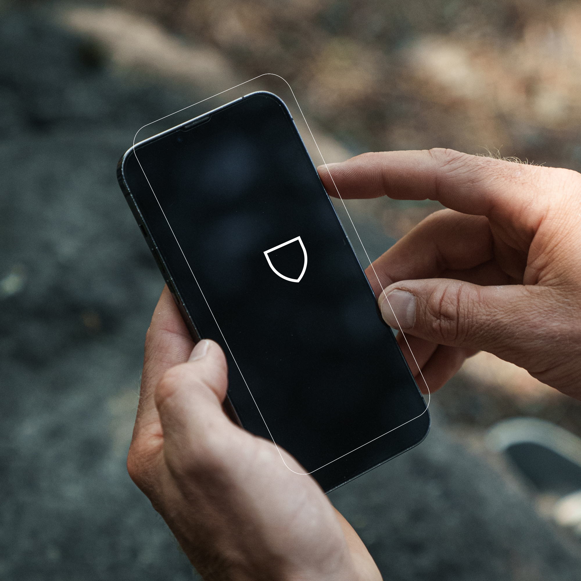 Ręka trzymająca smartfon z ochraniaczem ekranu. Na ekranie ikona tarczy.