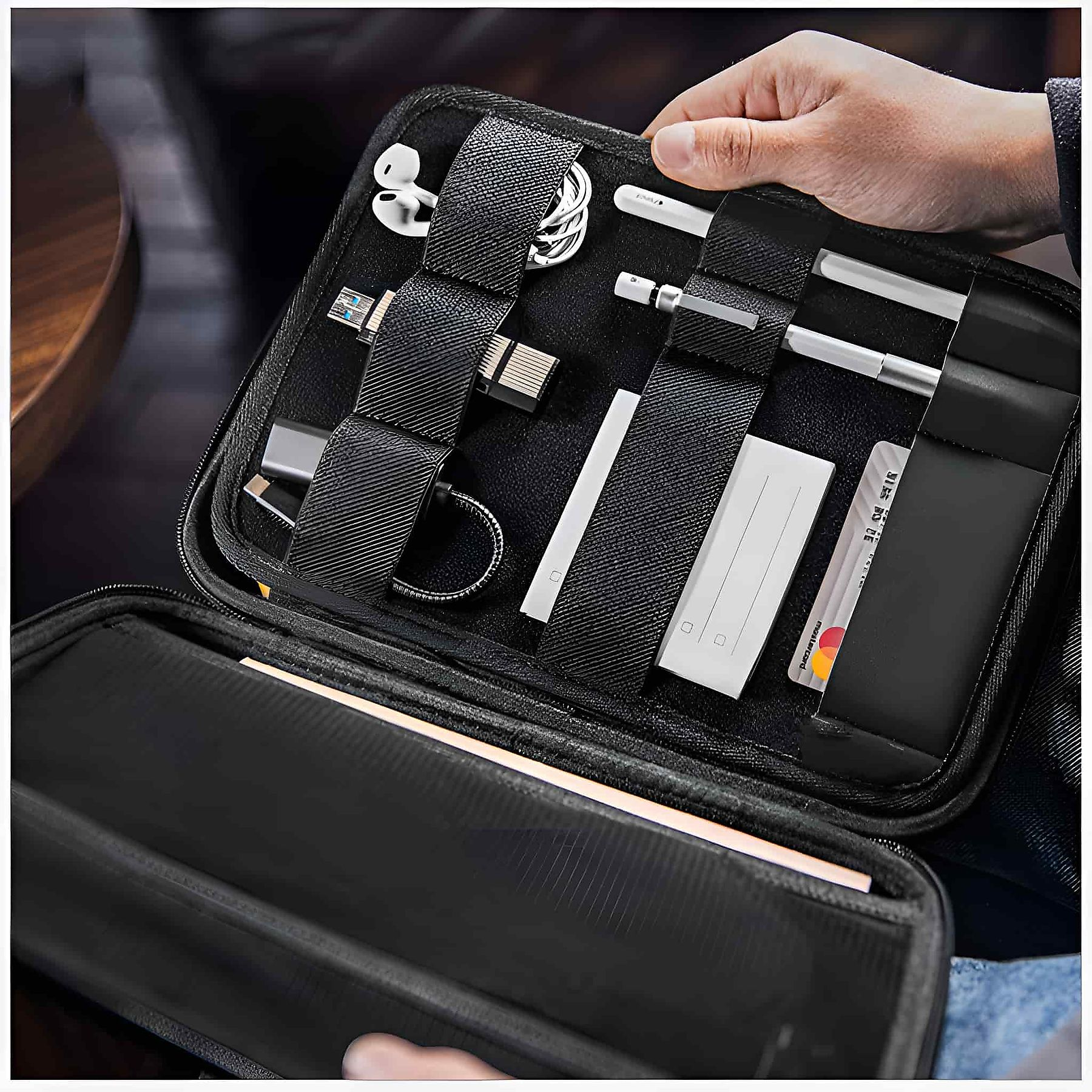 Geöffnete schwarze Reisetasche mit organisiertem Tech-Zubehör: Kabel, Stifte und Karten.