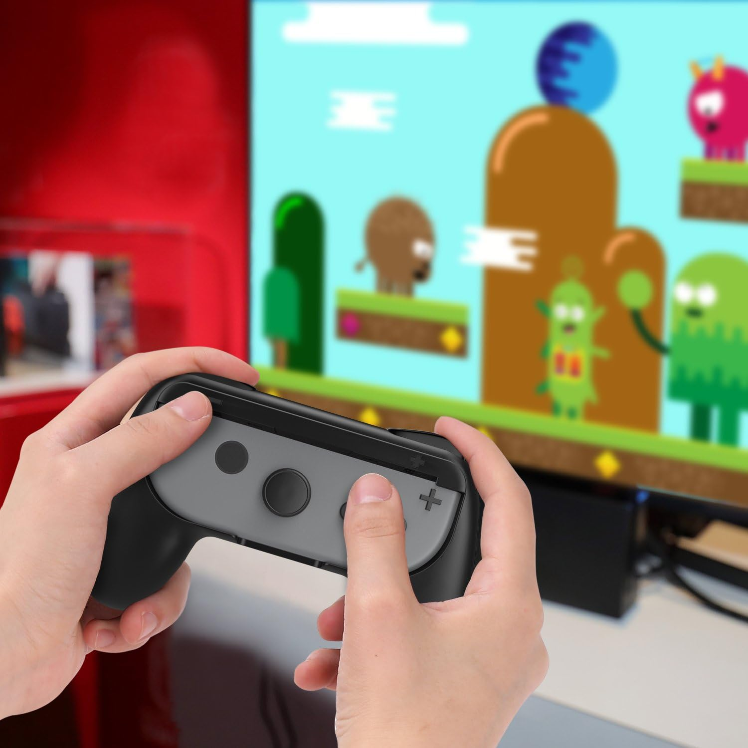 Hände halten einen Gamecontroller und spielen ein Spiel auf einem Monitor. Ein Cartoon-Spiel wird auf dem Bildschirm angezeigt.