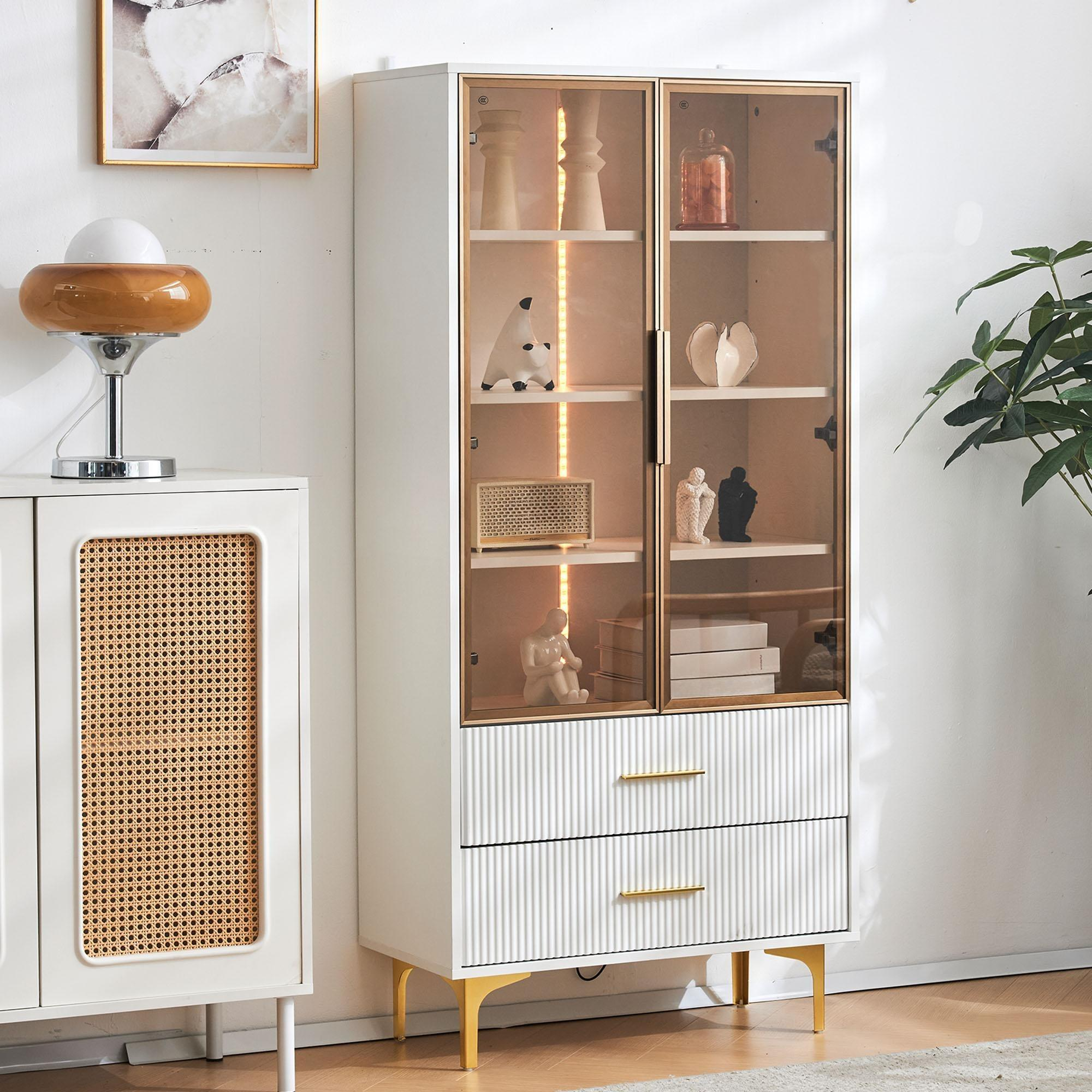 Weißer Schrank mit Glastüren, der Dekorationsgegenstände zeigt. Goldakzente und eine Lampe sind sichtbar.