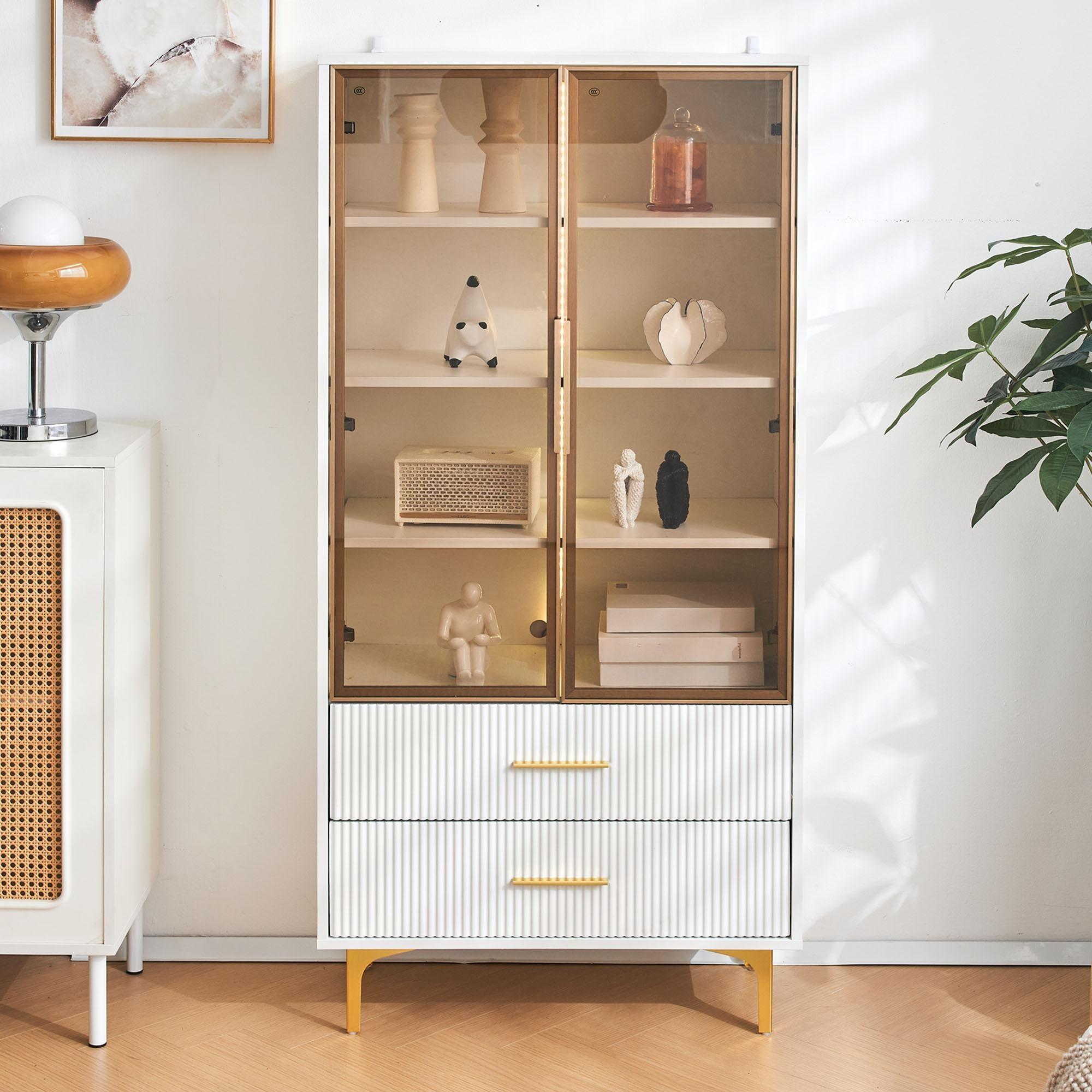 Weißer Schrank mit Glastüren, Innendetails und Dekorationsgegenständen. Eine Lampe und eine Pflanze sind ebenfalls sichtbar.