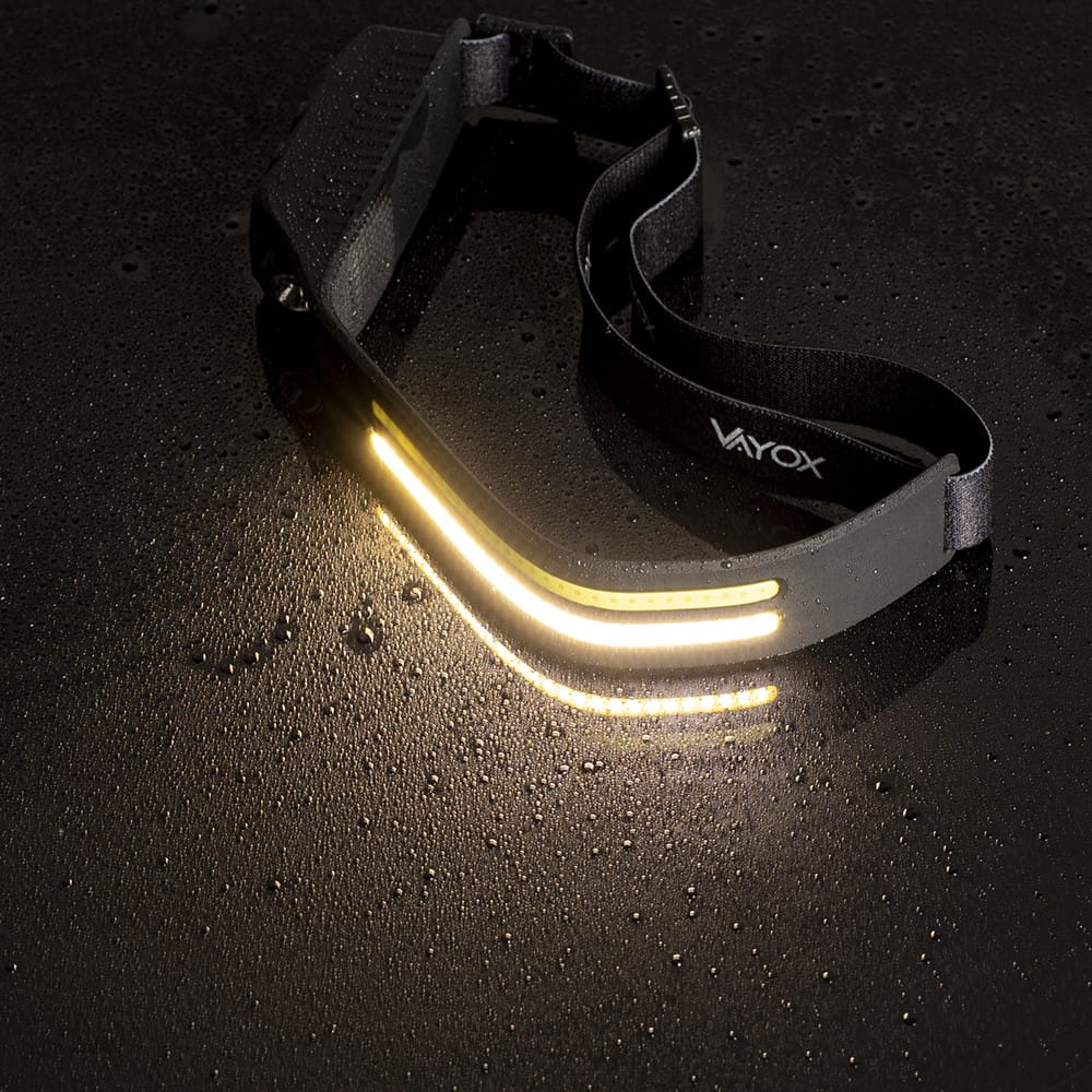 Latarka czołowa. Czarna z żółtym paskiem i jasnym światłem świecącym na mokrej powierzchni.